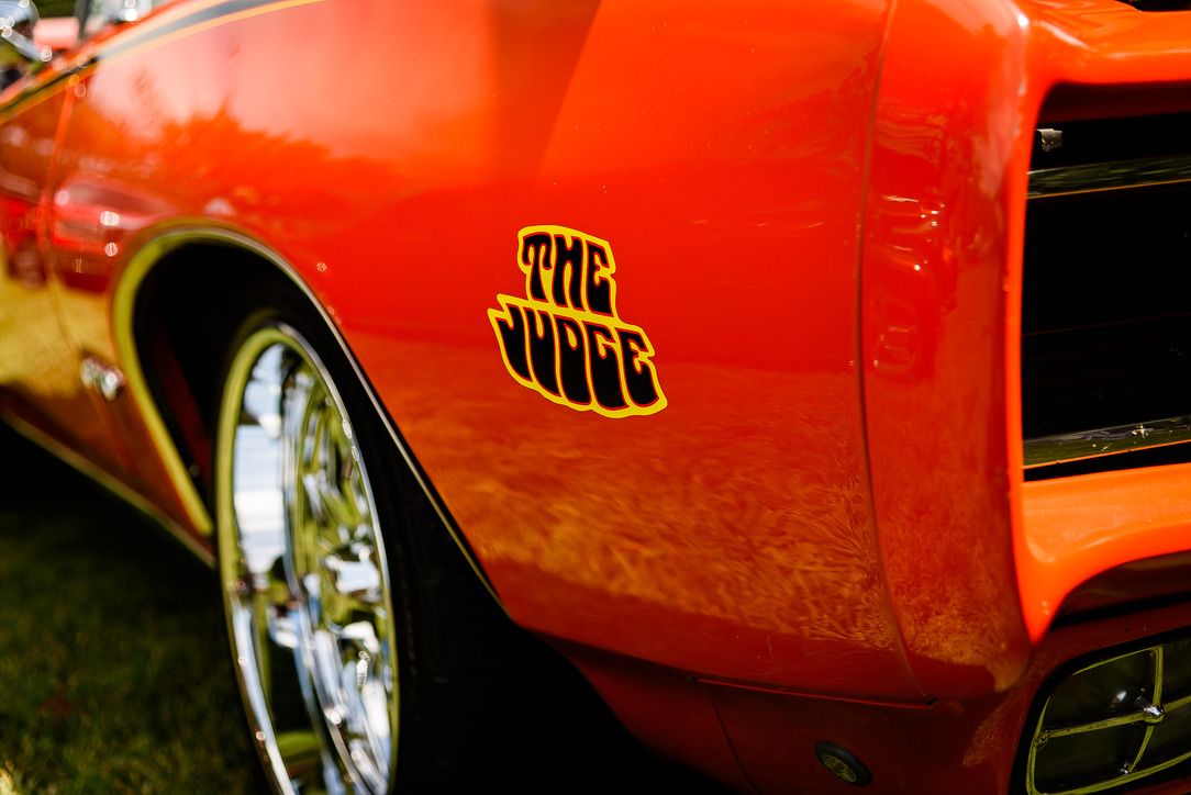 Close-up of a red Pontiac GTO Judge muscle car showcasing chrome wheel and iconic The Judge emblem.