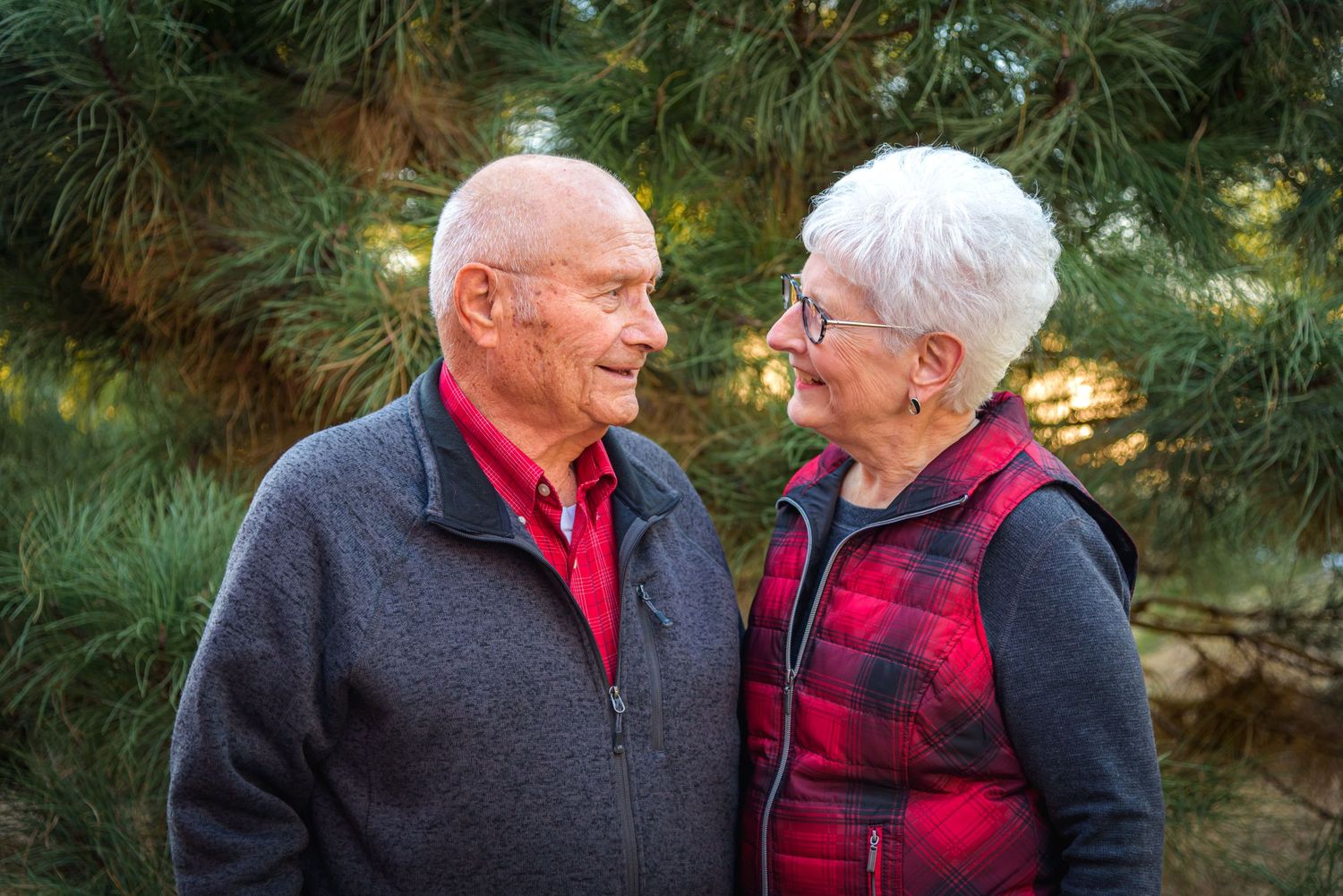Elderly couple sharing a loving glance outdoors near green pine trees. Polk County, NE