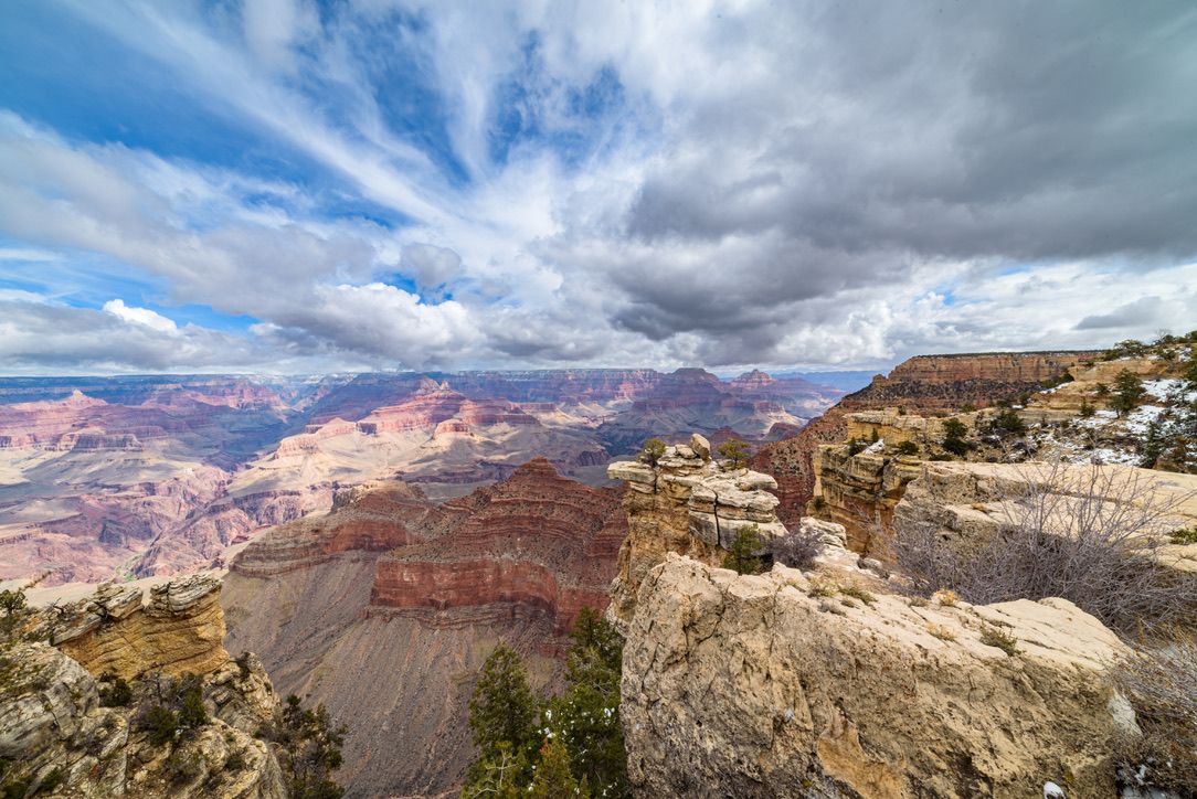 Panoramic view of the Grand Canyon with layered red rock formations under a dramatic cloudy sky.