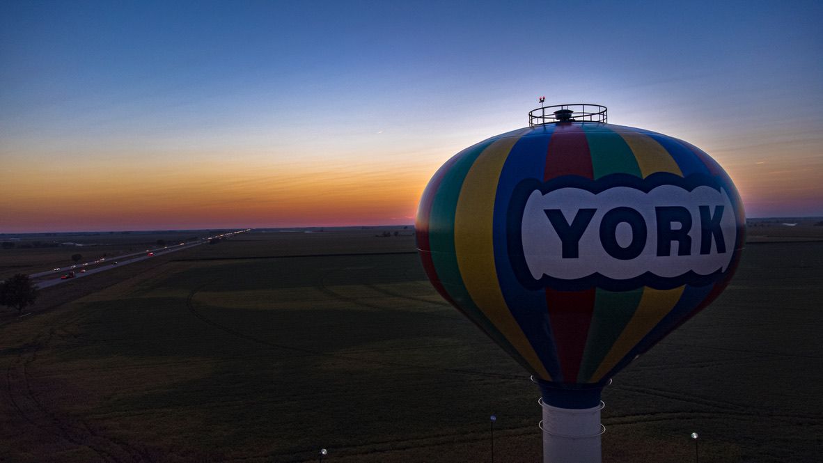Colorful hot air balloon-shaped water tower with YORK text against a stunning sunset sky over flat farmland.