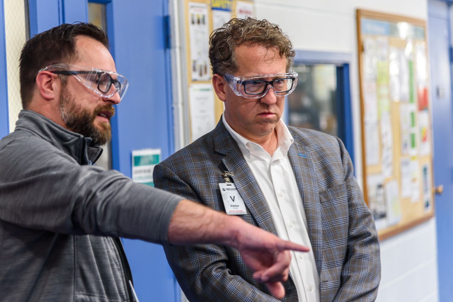 Two professionals wearing safety glasses discuss work in a modern industrial facility.