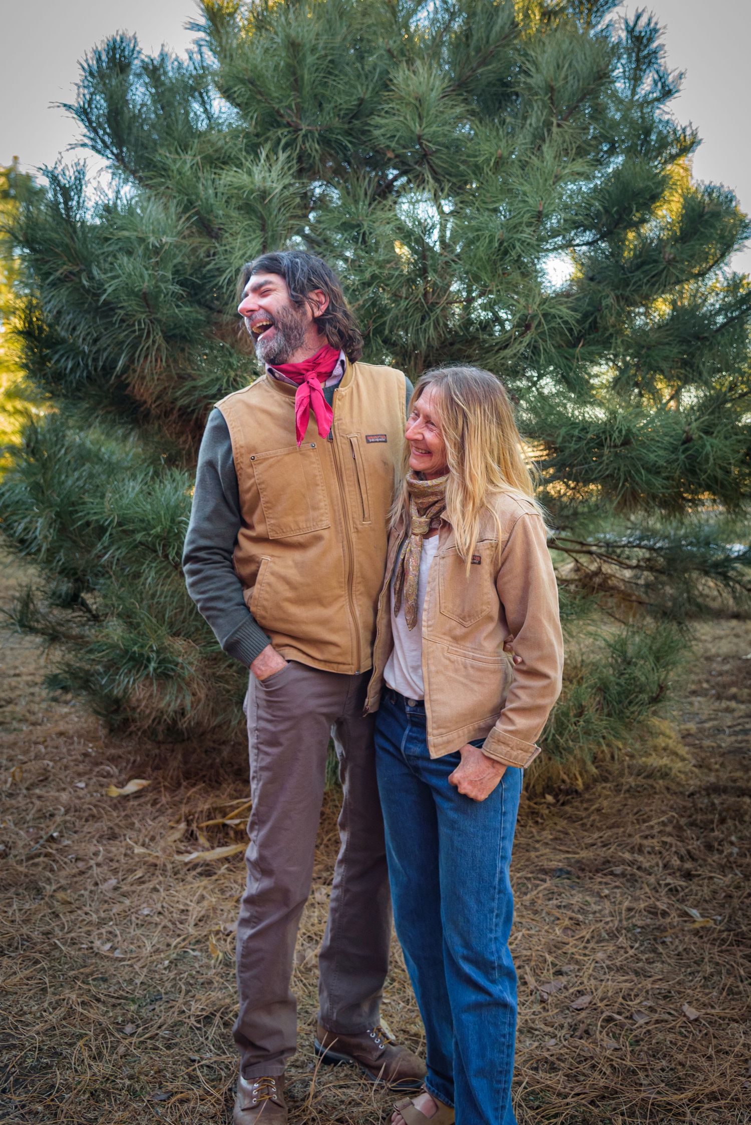 Happy couple laughing together outdoors in front of a green pine tree. Polk County, NE