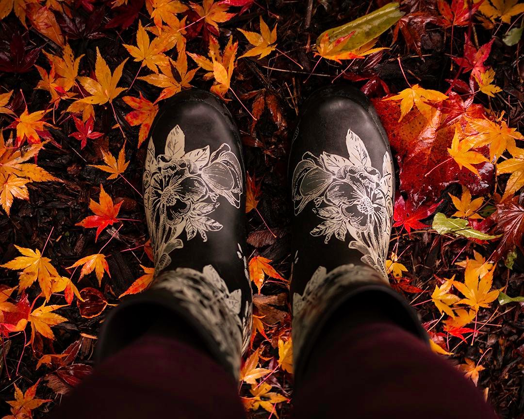 Black boots with floral embroidery surrounded by vibrant red and orange autumn leaves on the ground.