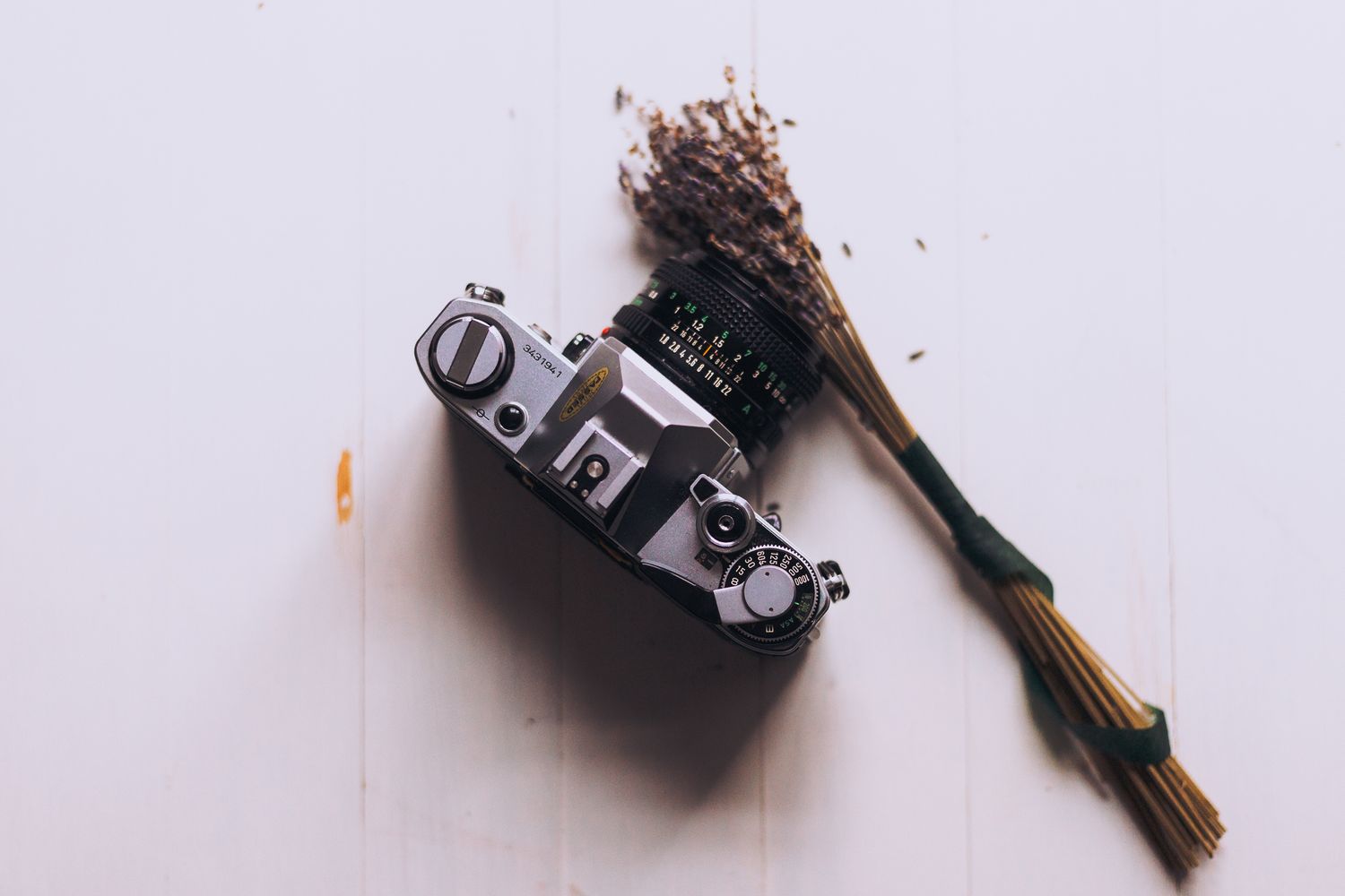 Vintage film camera with dried lavender flowers on a white wooden surface, flat lay photography.