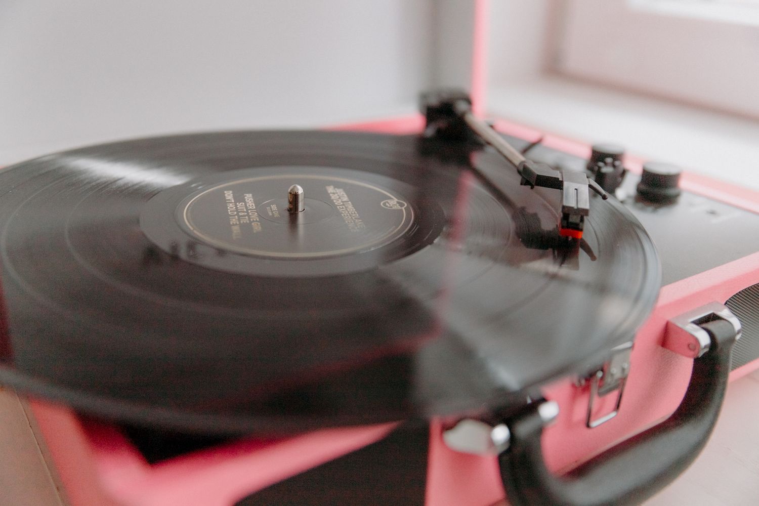 A black vinyl record spinning on a pink portable turntable record player on a white surface.