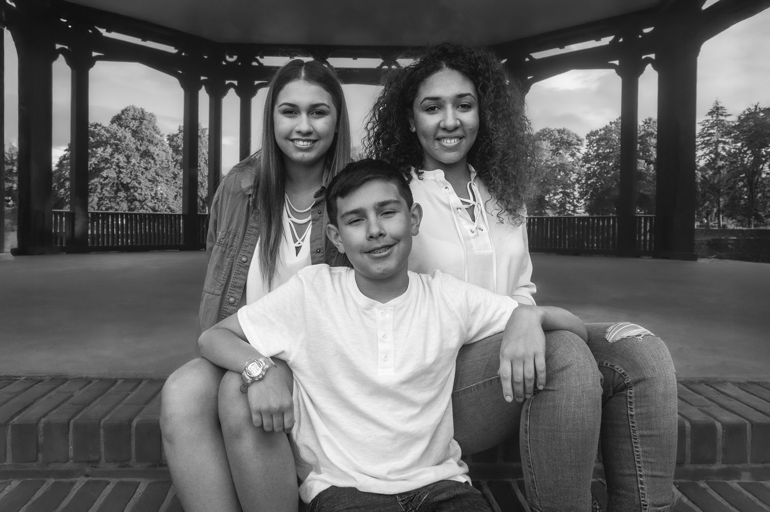 Three young friends pose together under a gazebo in a black and white outdoor portrait photo.