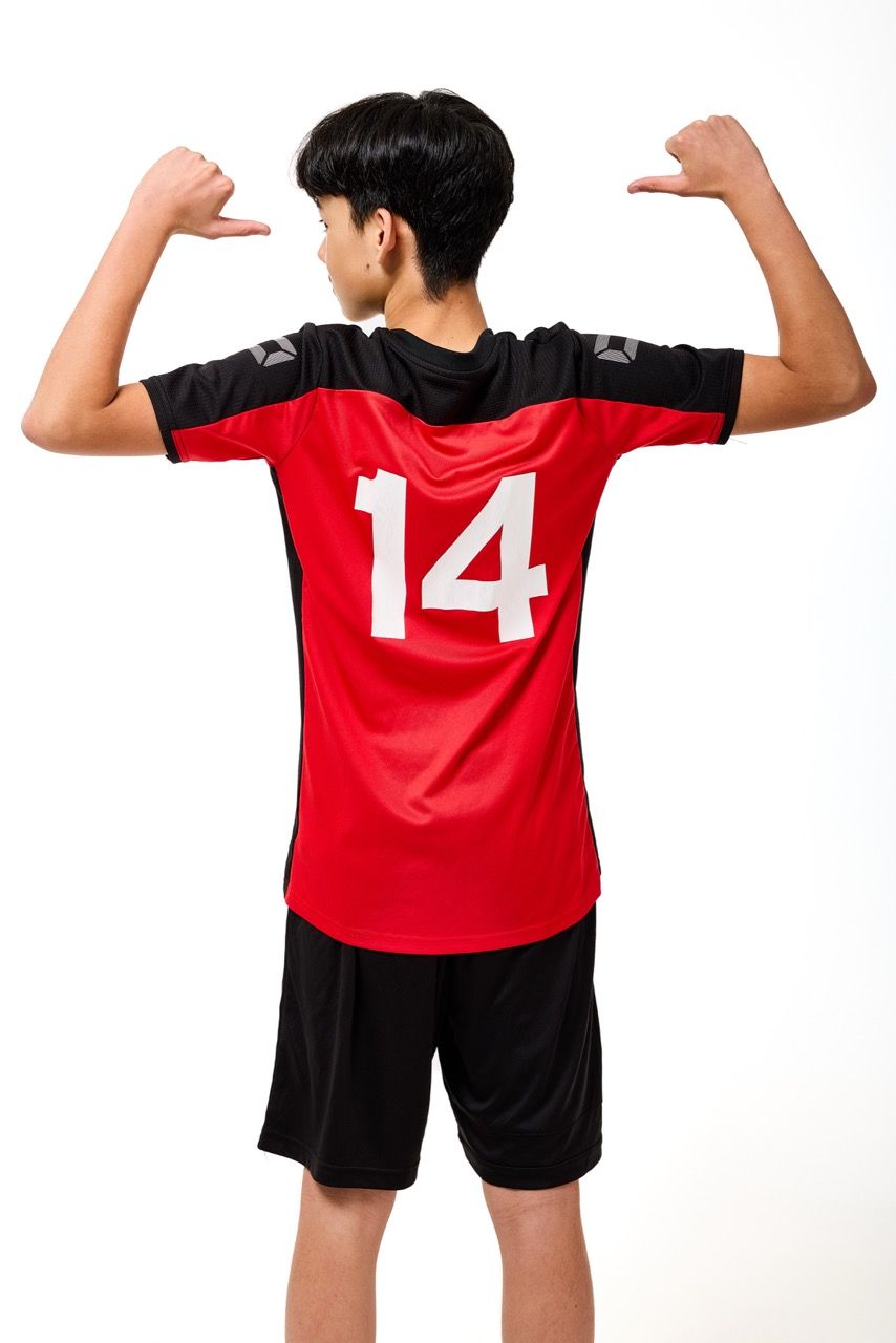 A young boy wearing a football kit, posing with a football against a clean white studio background.