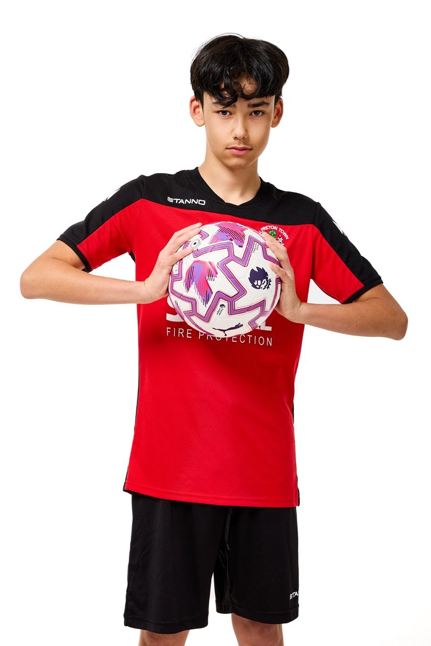 A young boy wearing a football kit and holding a ball, posing with a football against a clean white studio background.