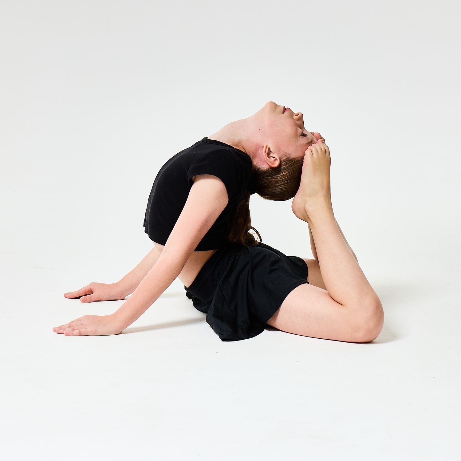 A modern dancer wearing a black vest top and shorts, captured in a sharp, athletic pose against a clean white background.