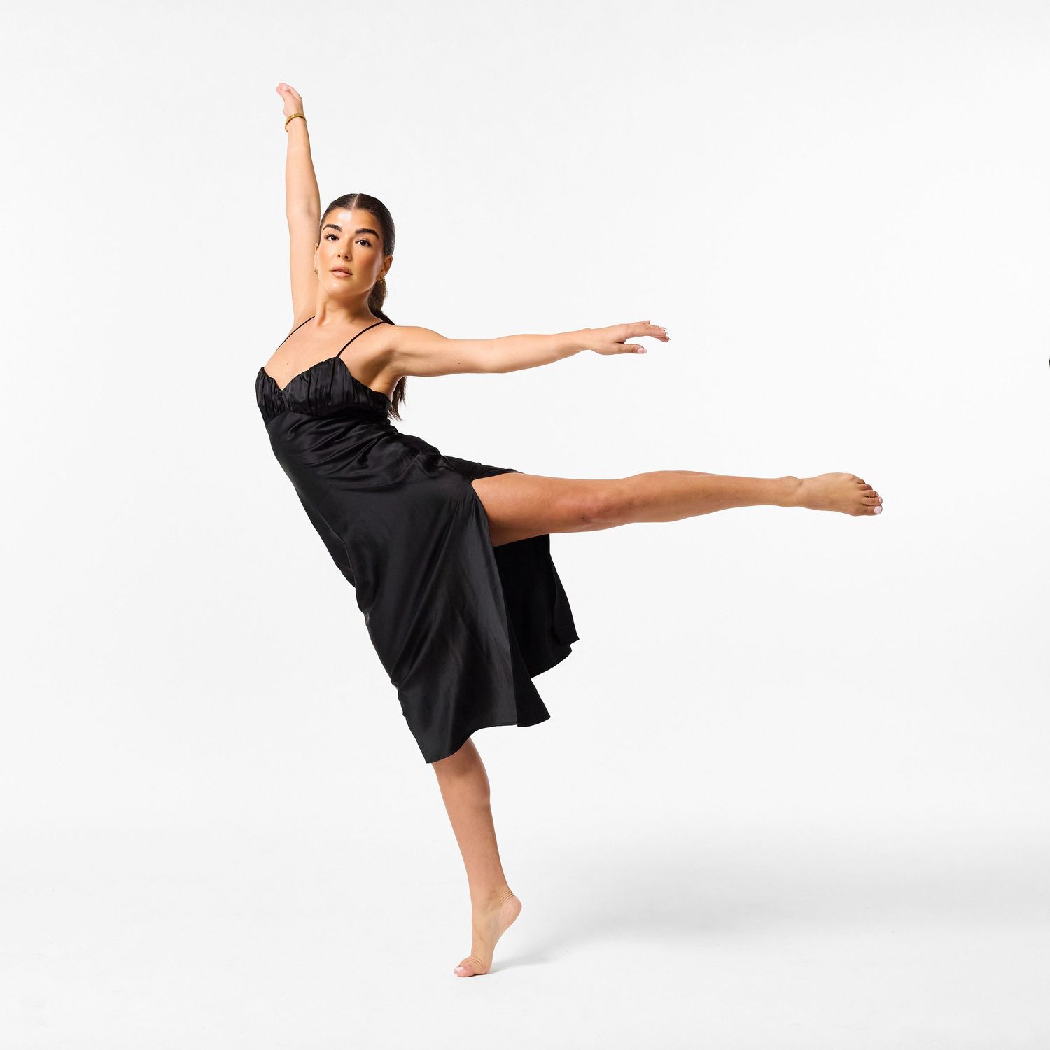 A classical dancer in an elegant black dress, captured in a graceful, fluid movement against a clean white background.