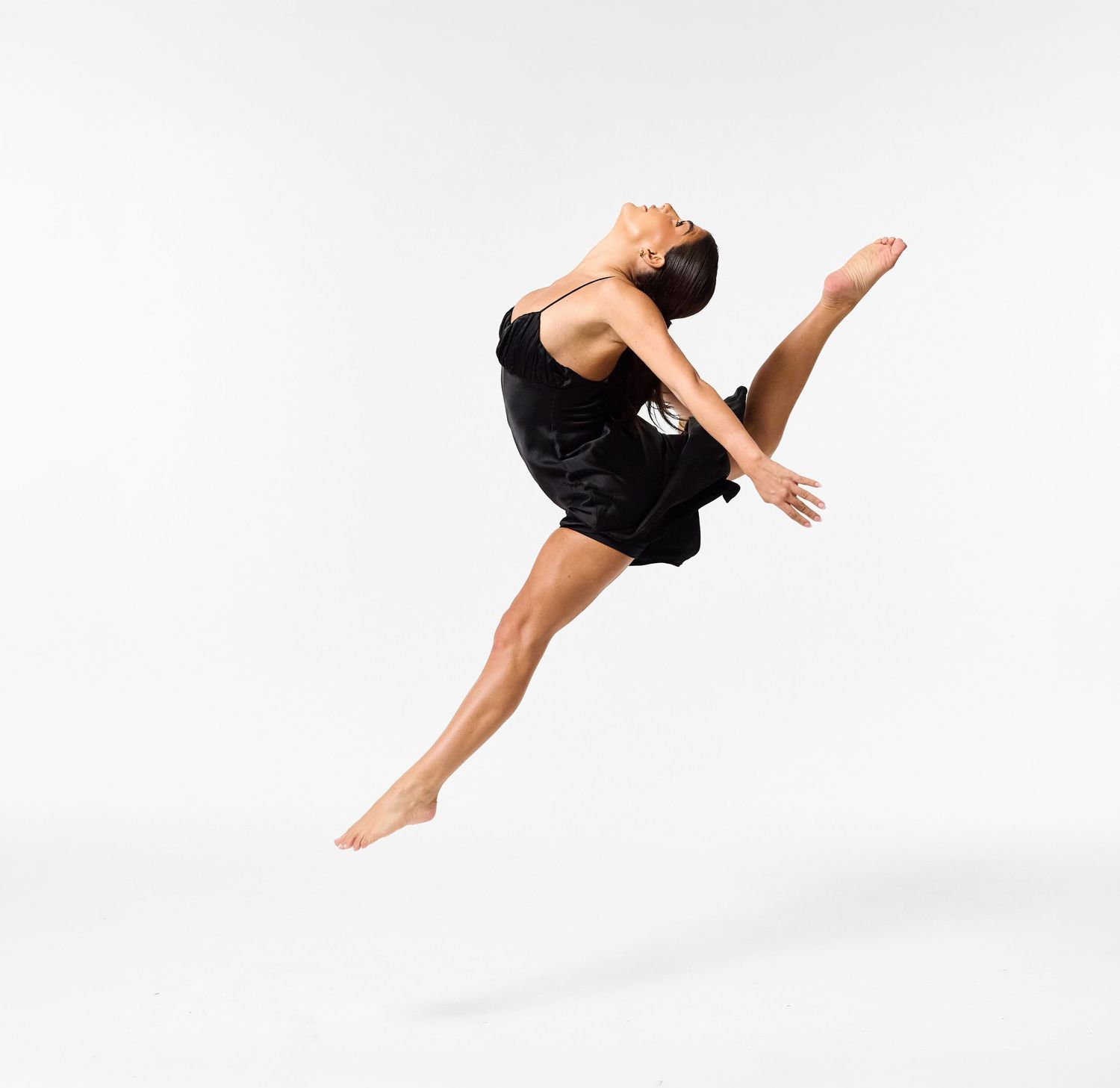 A classical dancer in an elegant black dress, captured in a graceful, fluid movement against a clean white background.