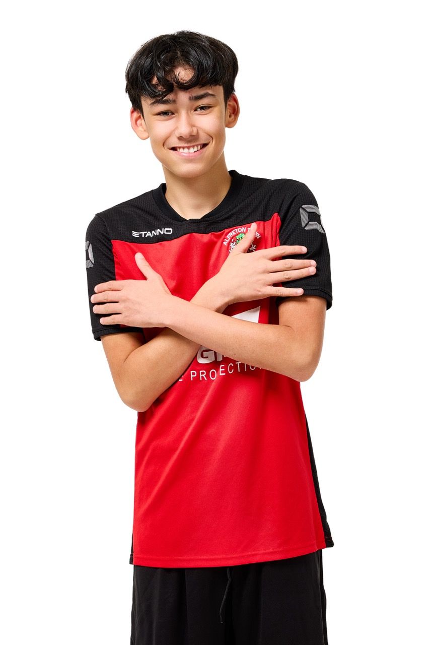 A young boy wearing a football kit, posing with a football against a clean white studio background.