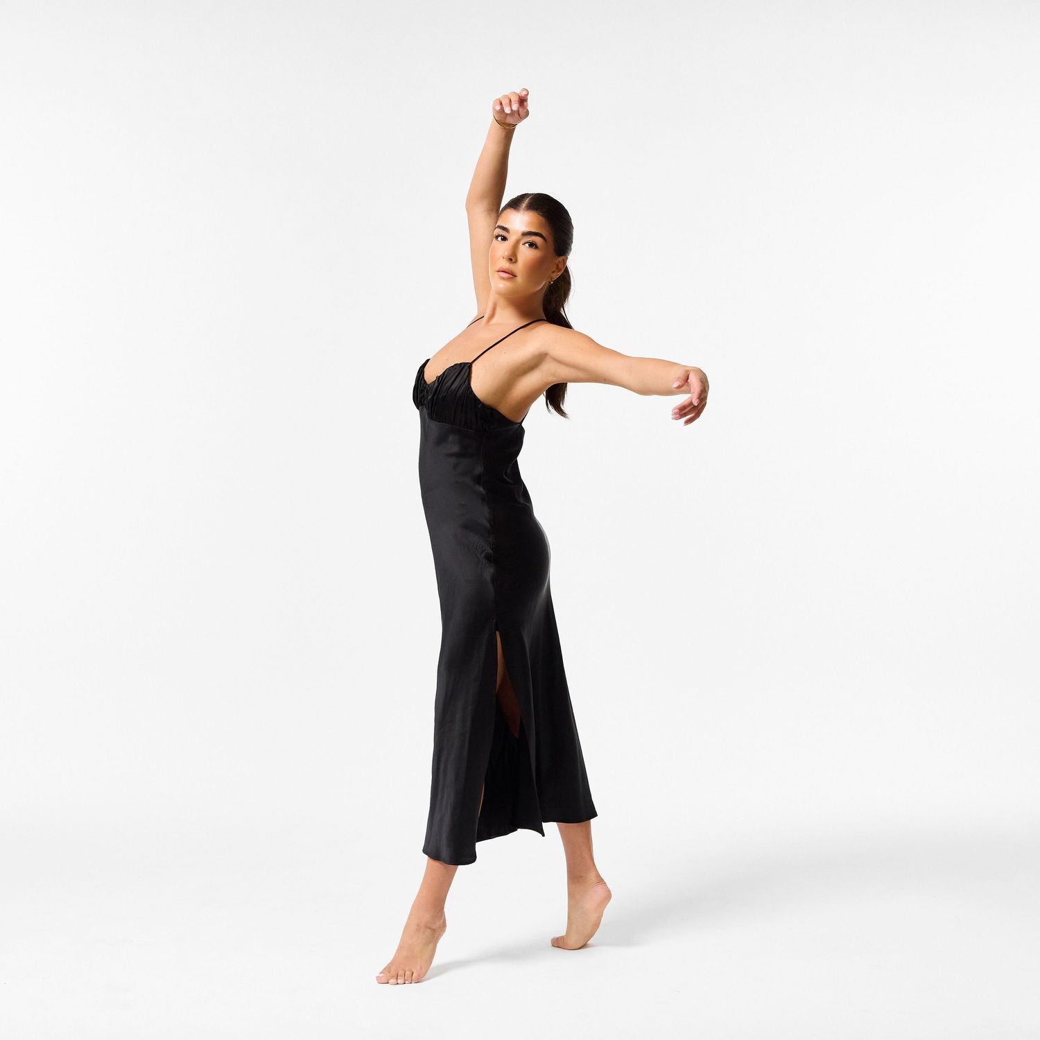 A classical dancer in an elegant black dress, captured in a graceful, fluid movement against a clean white background.