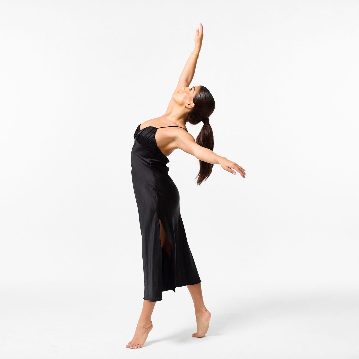 A classical dancer in an elegant black dress, captured in a graceful, fluid movement against a clean white background.