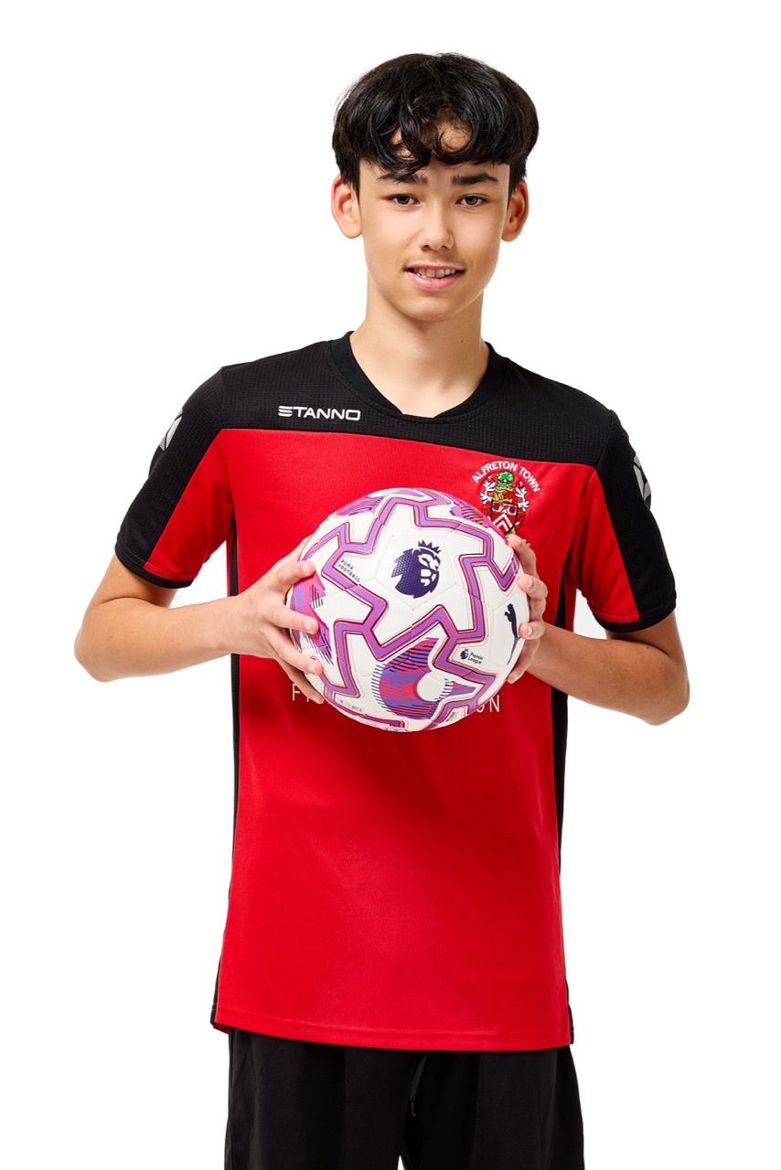 A young boy wearing a football kit and holding a ball, posing with a football against a clean white studio background.