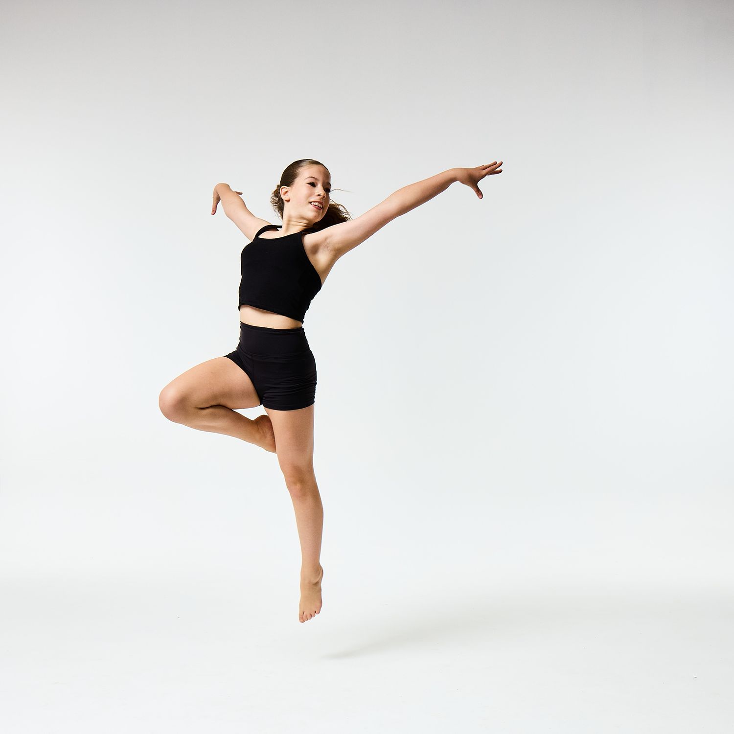 A modern dancer wearing a black vest top and shorts, captured in a sharp, athletic pose against a clean white background.