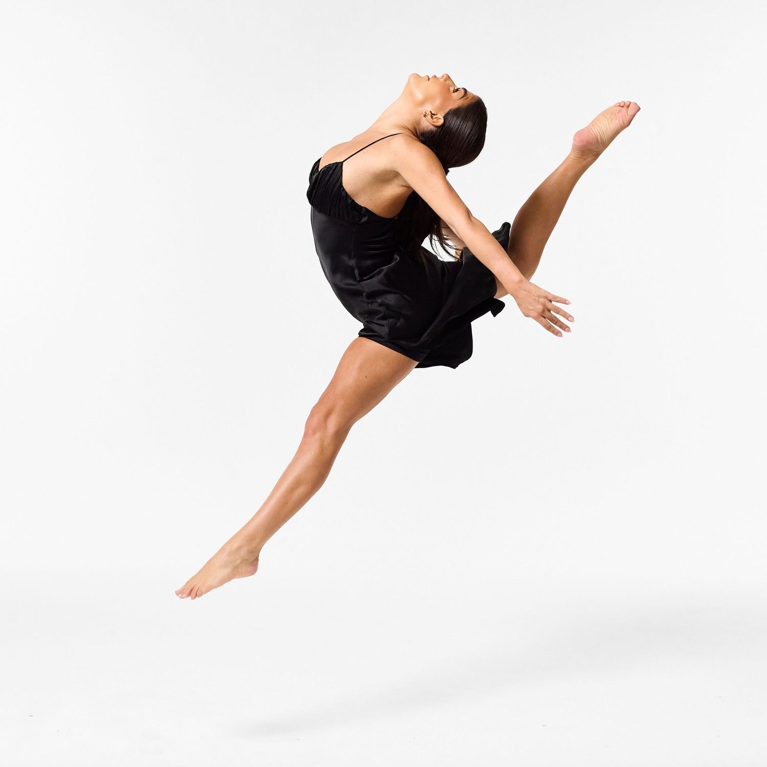 A classical dancer in an elegant black dress, captured in a graceful, fluid movement against a clean white background.