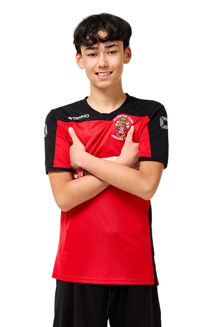 A young boy wearing a football kit, posing with a football against a clean white studio background.