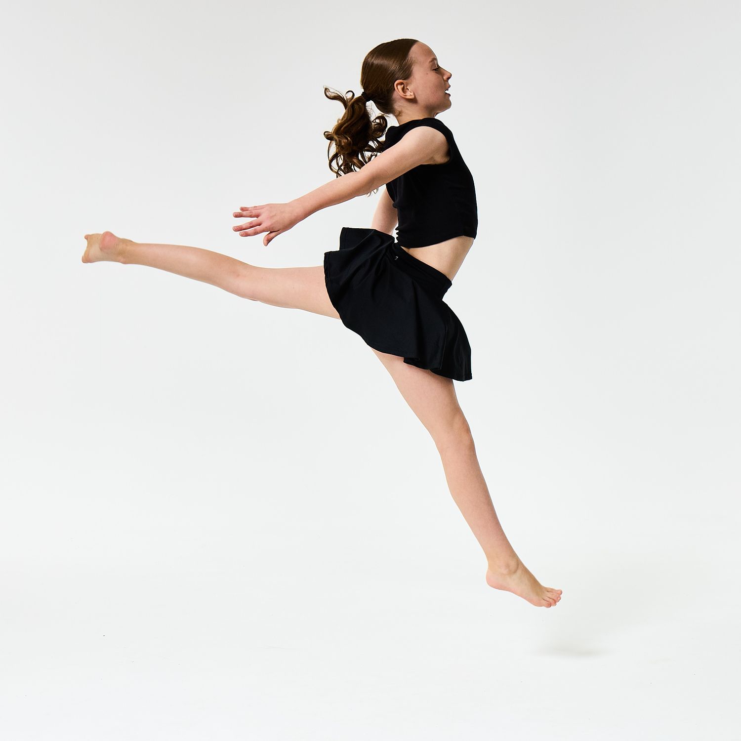 A modern dancer wearing a black vest top and shorts, captured in a sharp, athletic pose against a clean white background.