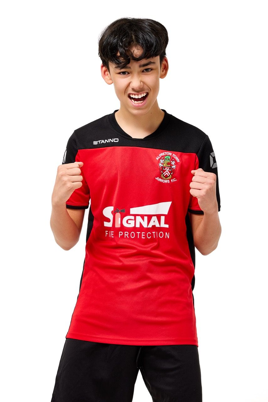A young boy wearing a football kit, posing with a football against a clean white studio background.