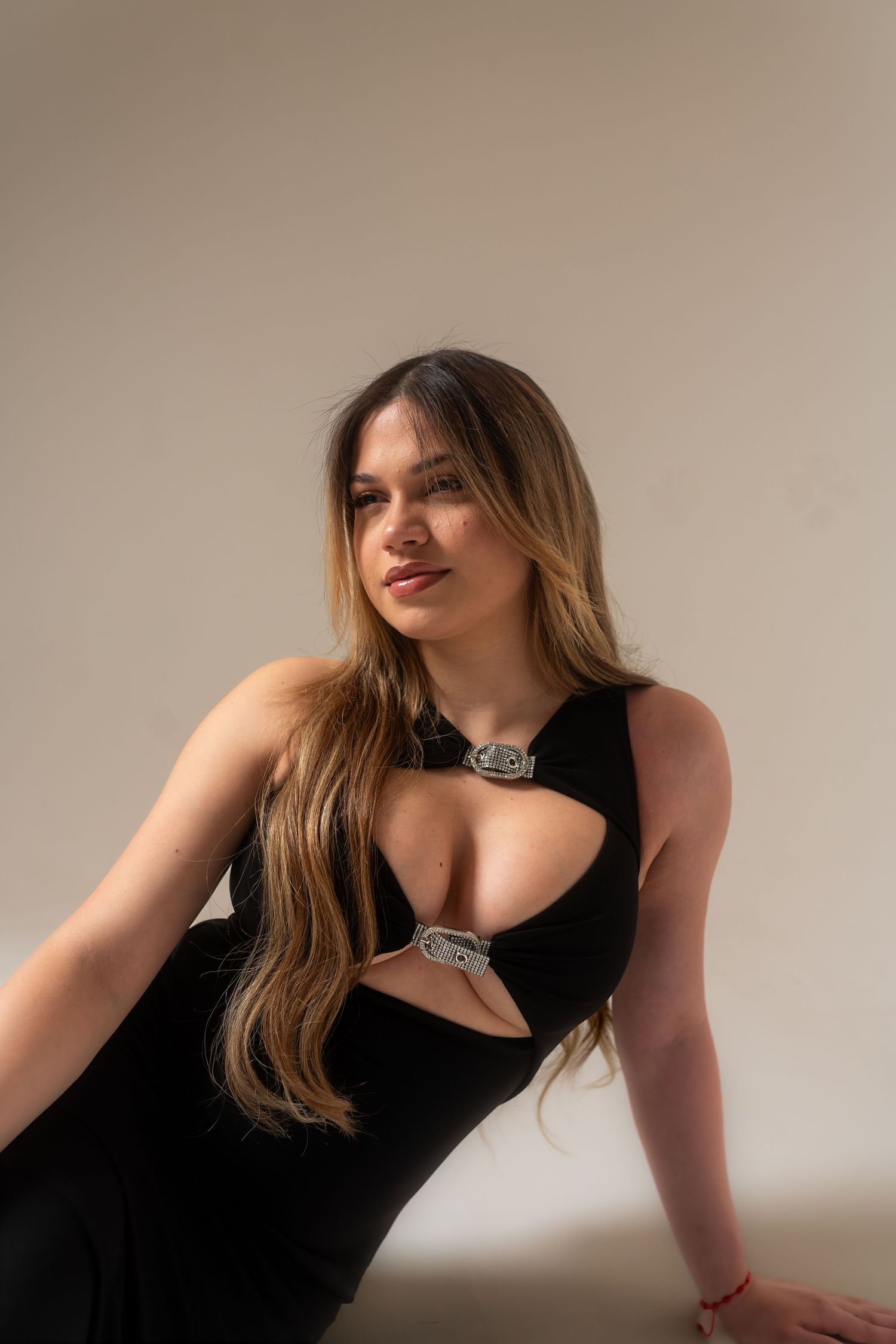 Woman in black cutout dress with silver buckle detail, posing against neutral background with long highlighted hair.