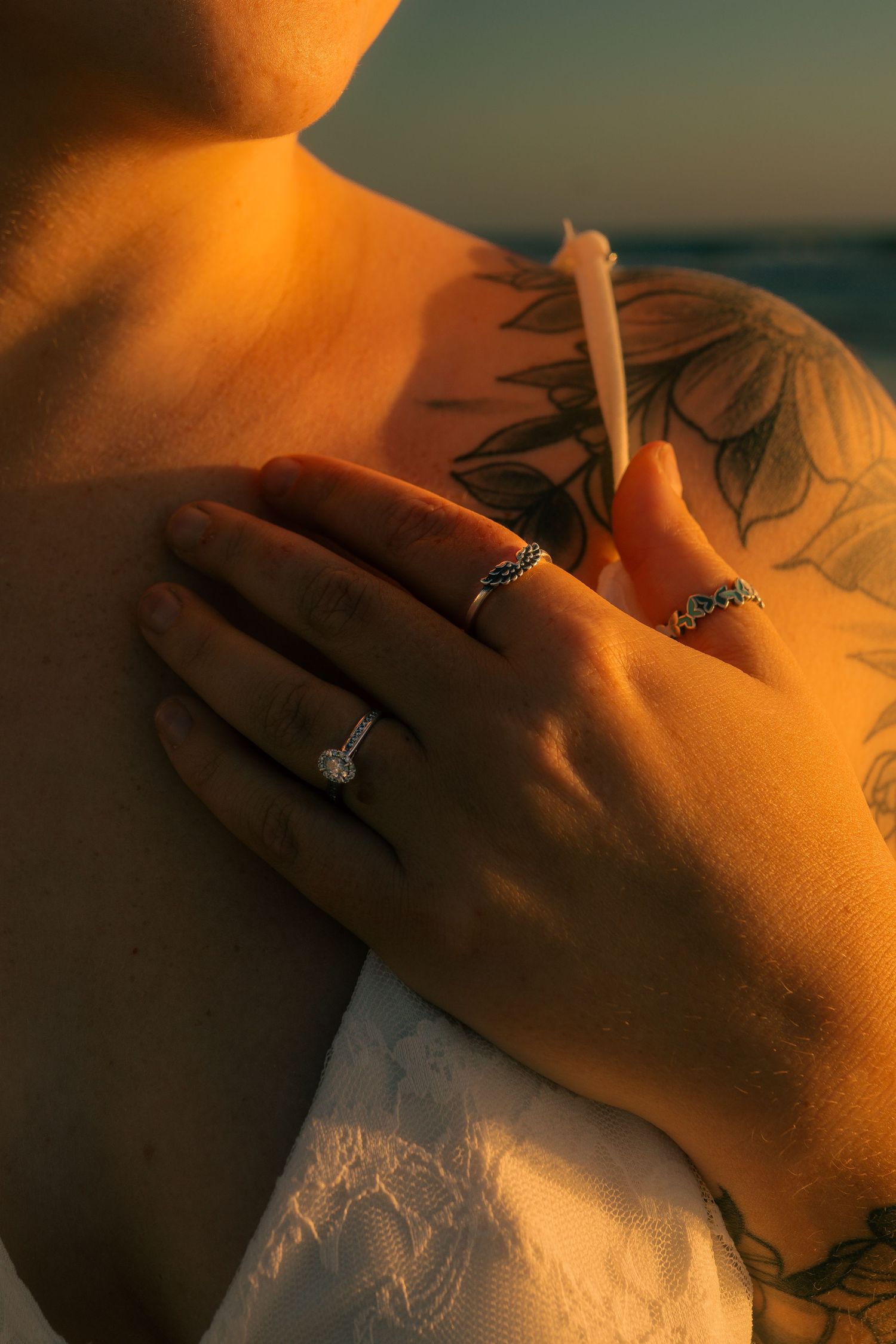 Close-up of hands with rings and tattoos embracing at golden sunset, romantic engagement photo.