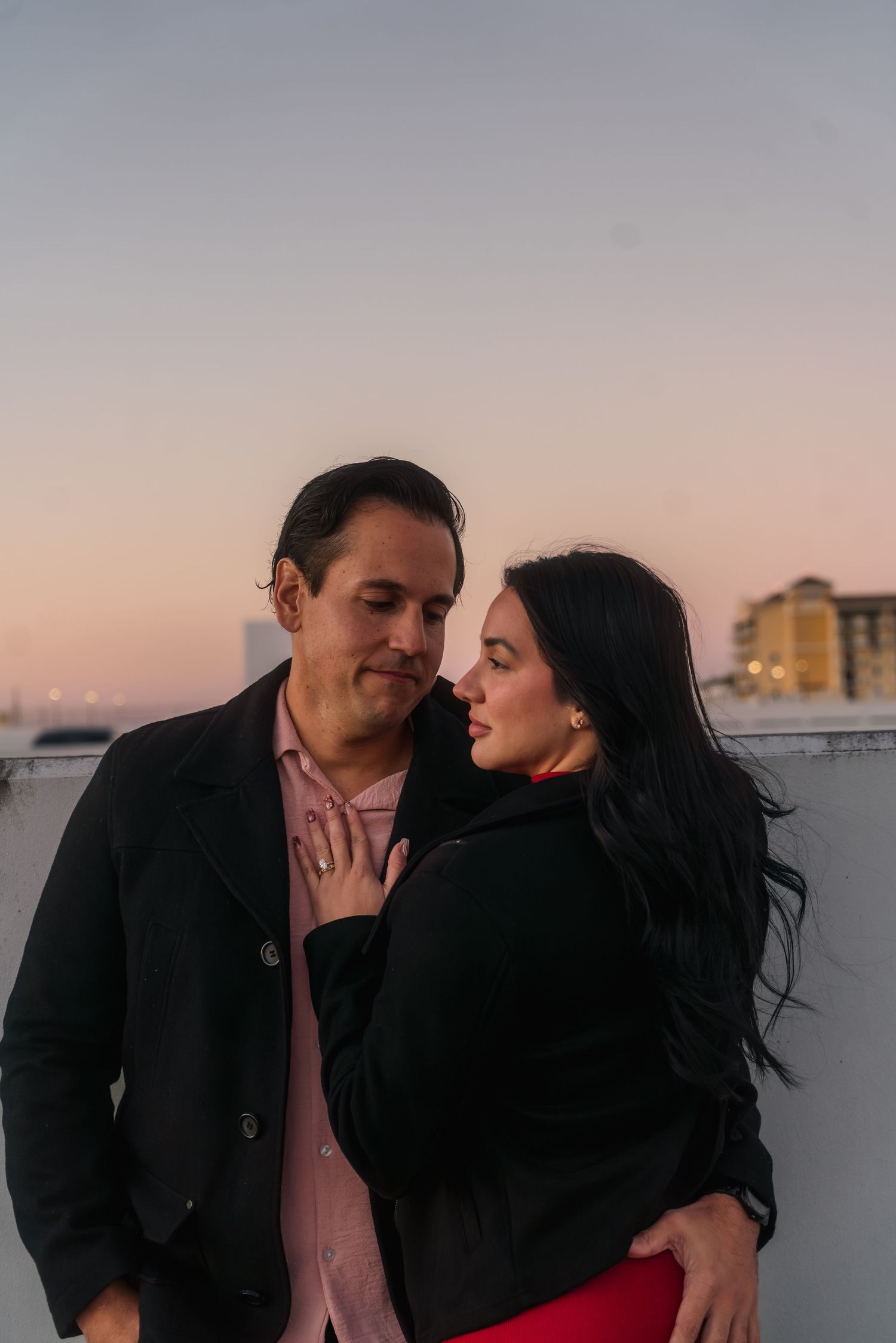 Couple sharing an intimate moment at sunset on a rooftop, woman in red dress leaning close to man.