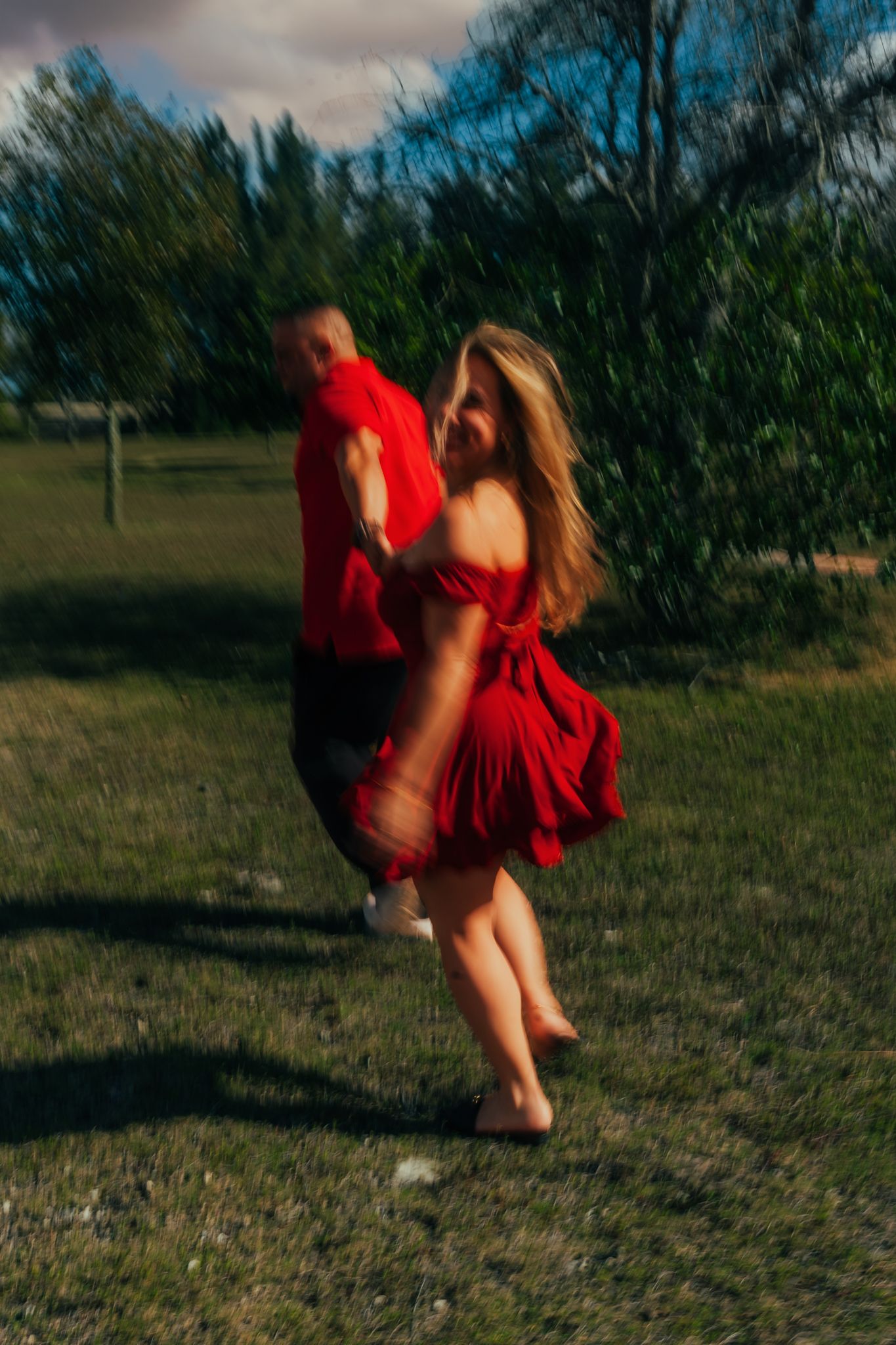 Blurred motion shot of couple in matching red outfits spinning playfully in a sunny green park.