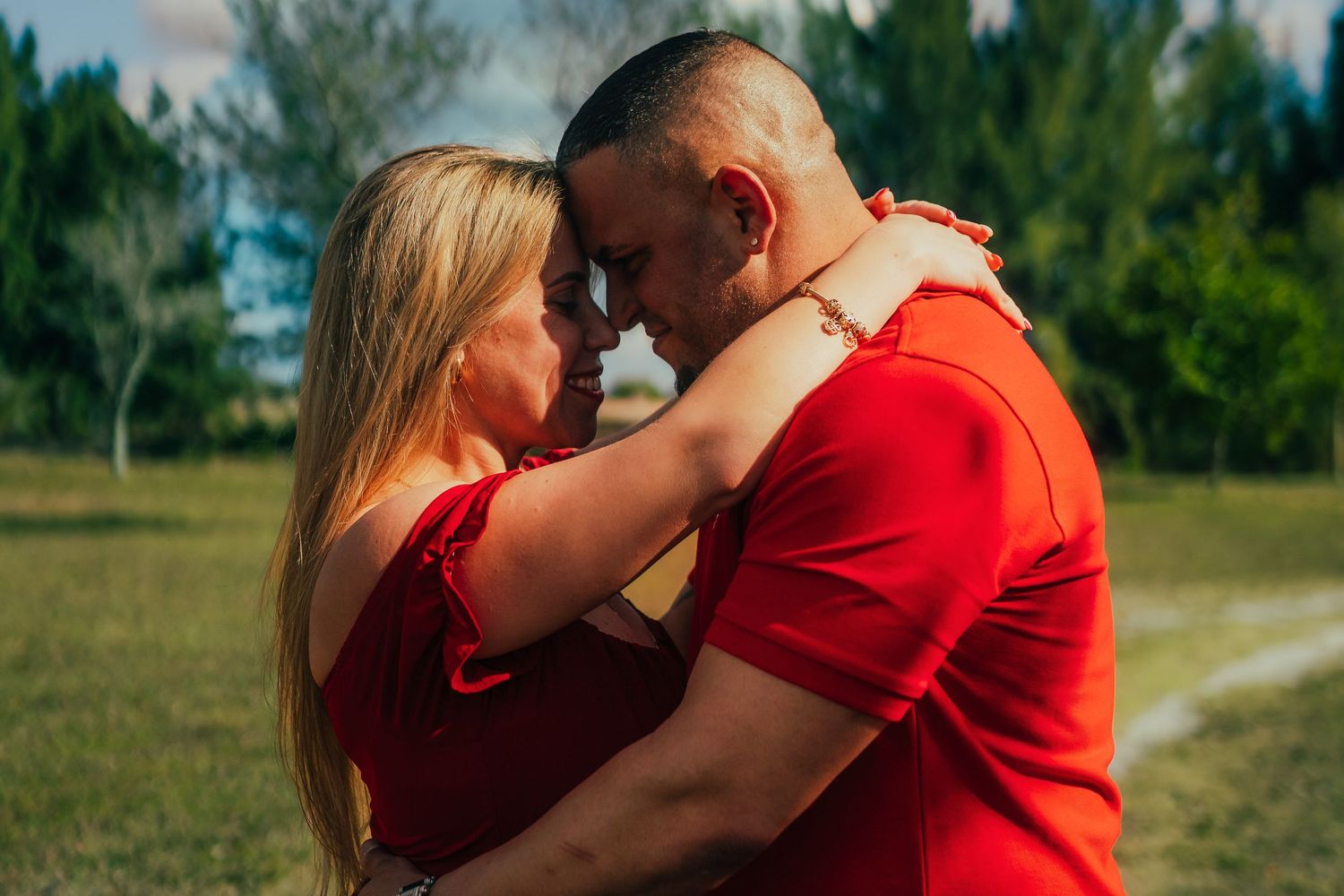 Couple in matching red outfits embracing forehead-to-forehead in a green field on a sunny day.