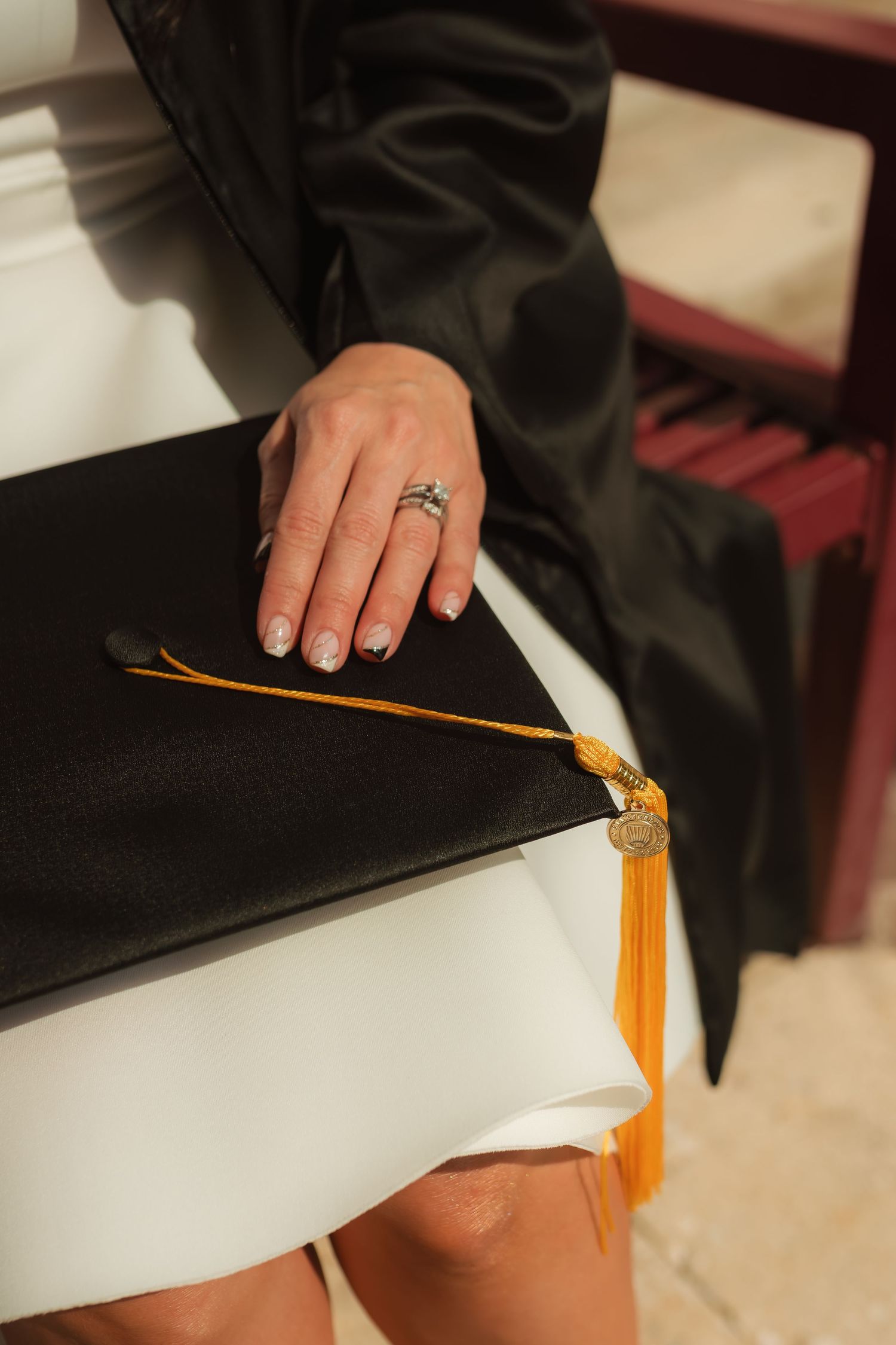 Close-up of graduate holding black mortarboard cap with gold tassel wearing graduation gown.
