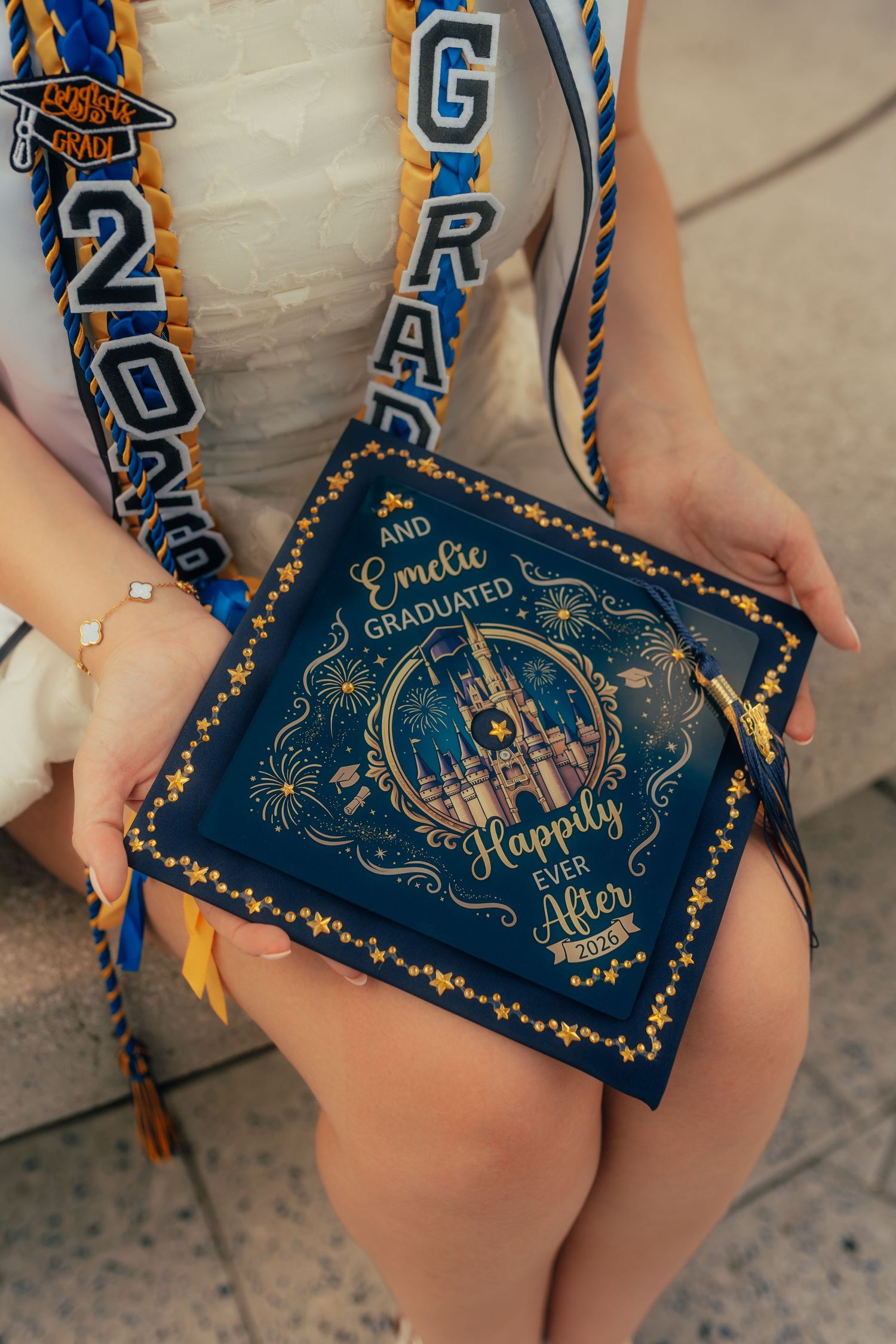 Graduate holding Disney-themed graduation cap reading 'And Emilie Graduated Happily Ever After 2024' with Cinderella Castle.