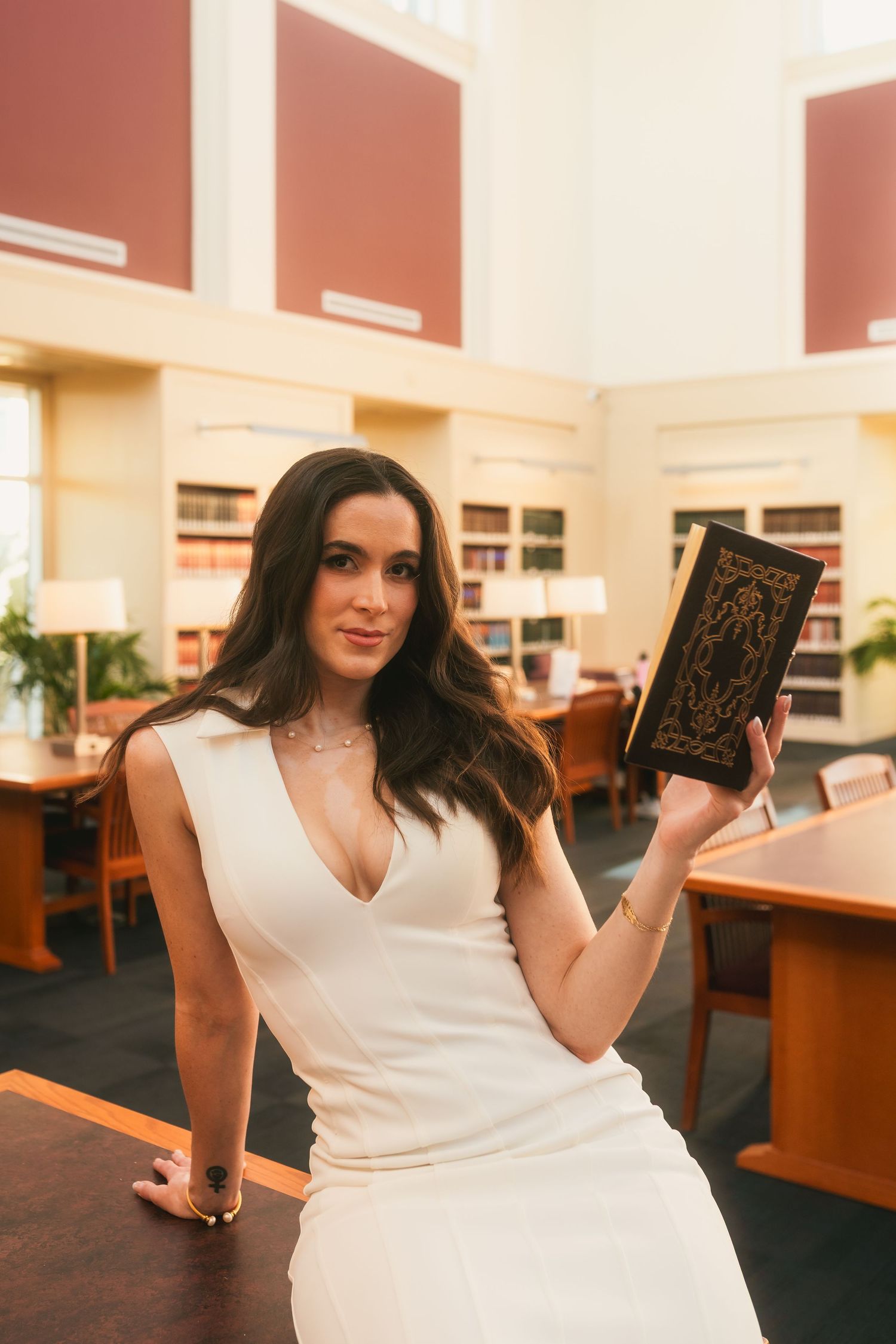 Woman in white dress holding an ornate book in an elegant library setting.