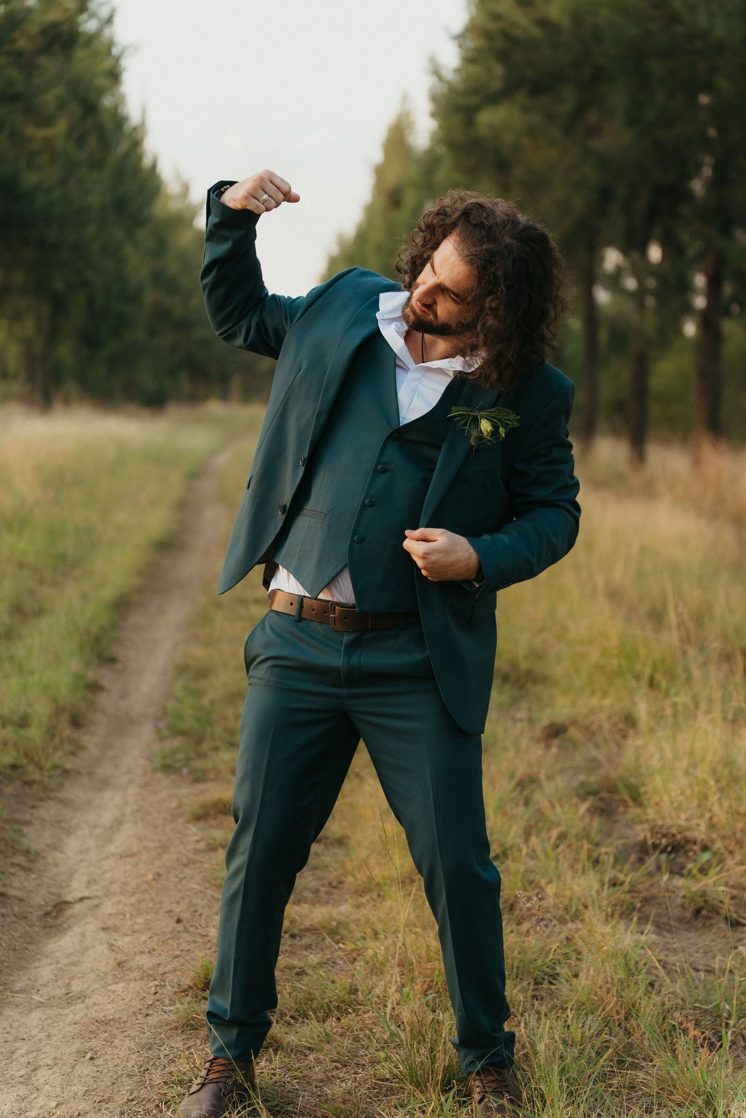 Man in green suit flexing on dirt path surrounded by trees.