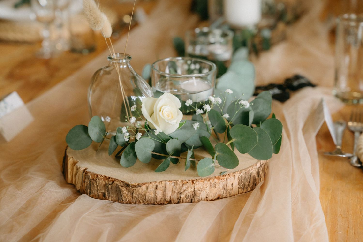 Rustic wedding centerpieces with wood slices, greenery and white flowers on table.