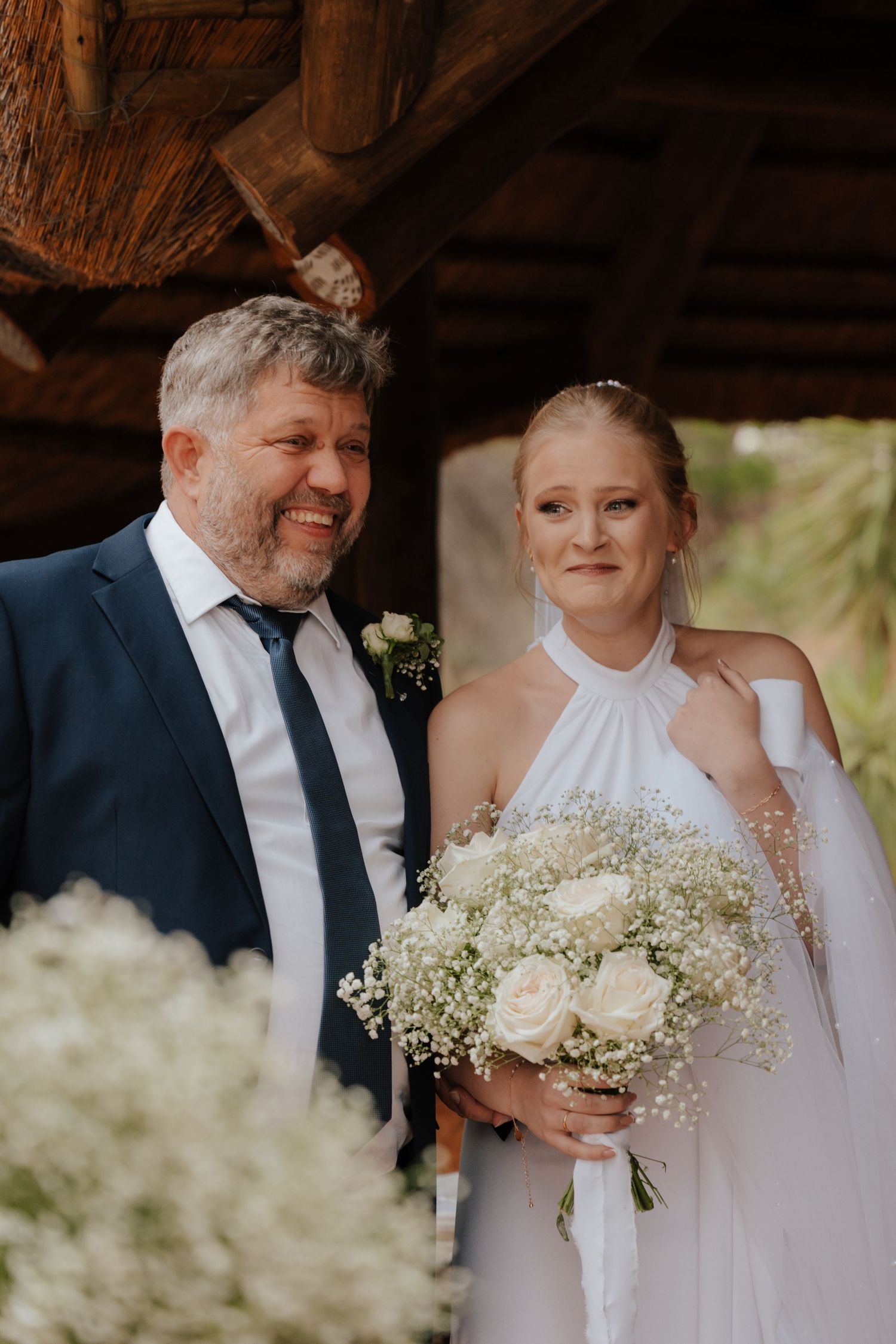 Wedding couple poses with white and green floral bouquet in a rustic barn setting.