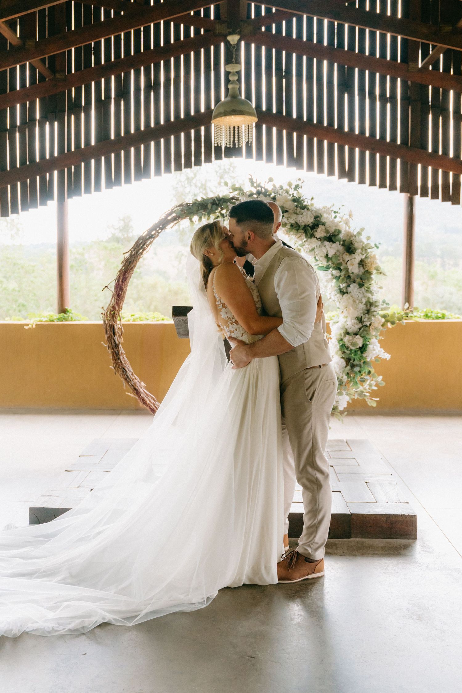 Romantic wedding couple sharing a moment under a wooden pavilion decorated with floral arch.
