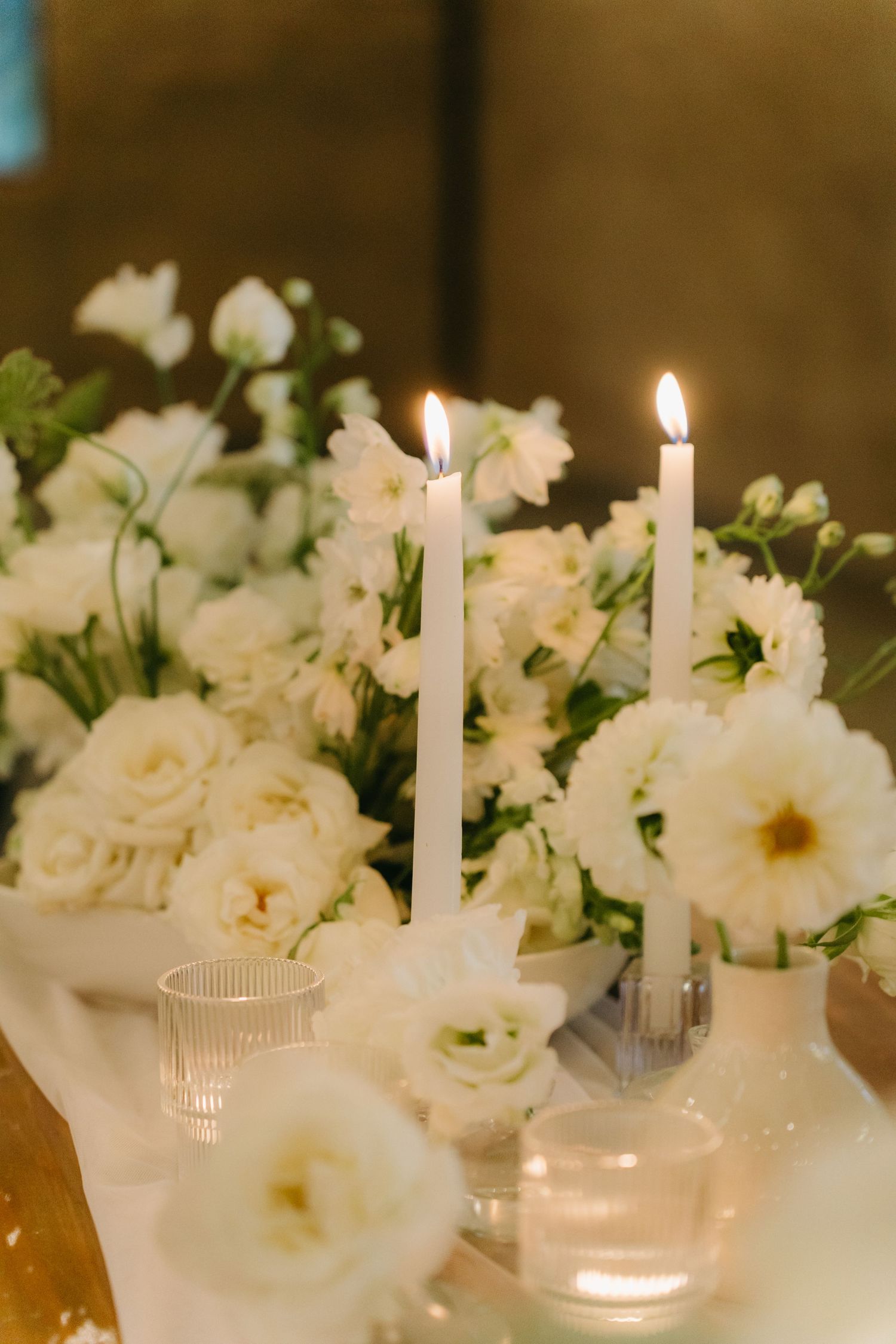 Elegant white floral centerpiece with lit taper candles on wedding reception table.