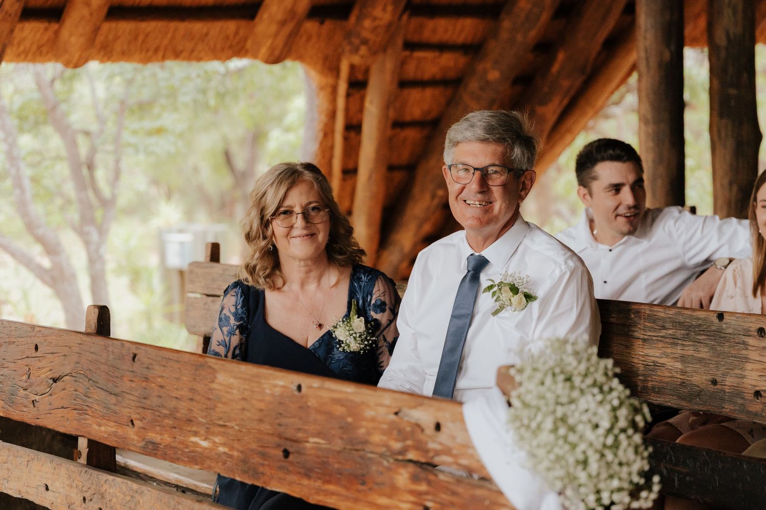 Wedding guests seated at rustic wooden tables decorated with baby's breath flowers.