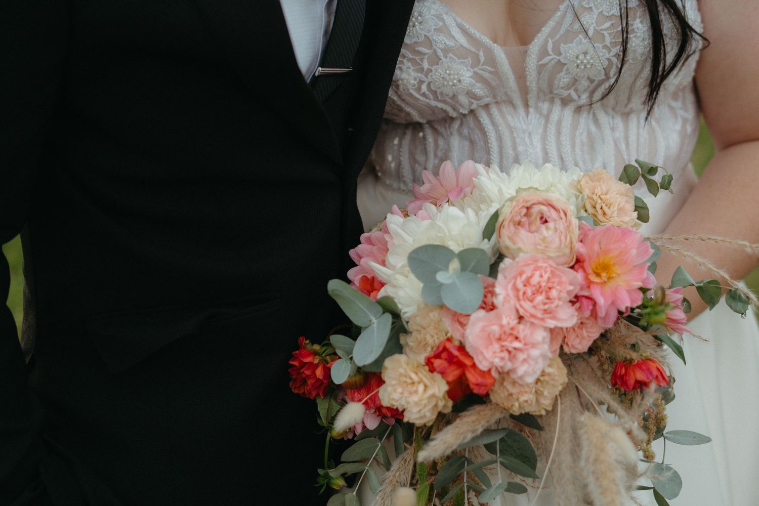 A close-up of a bride's pink and coral bouquet against formal wedding attire.