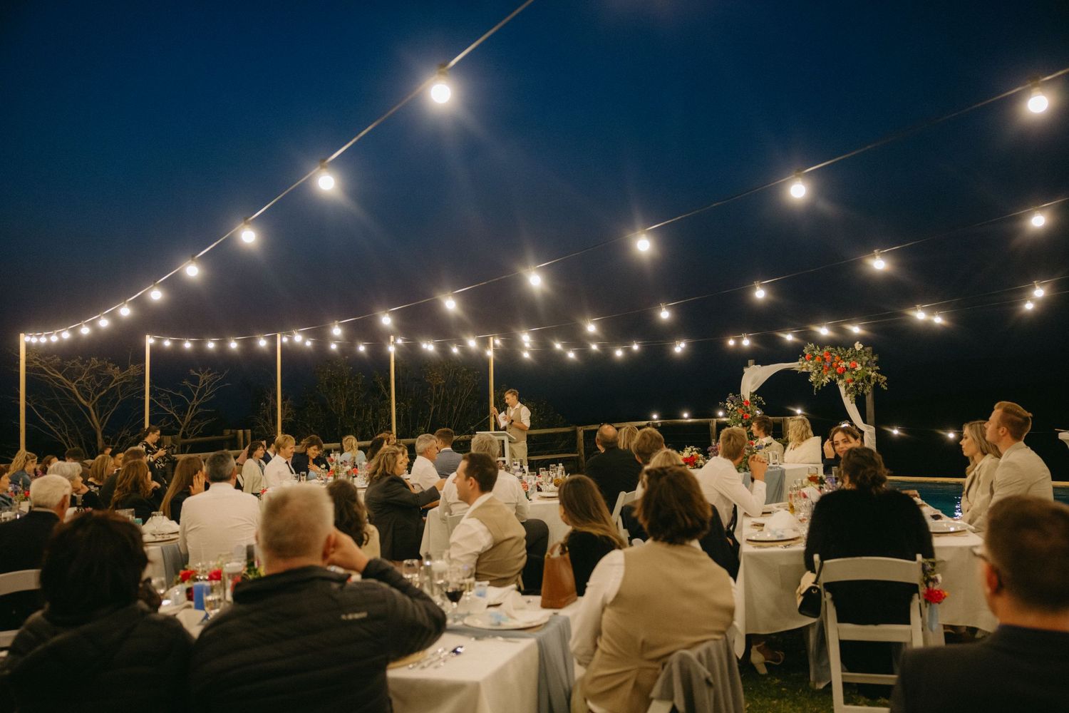 String lights illuminate an outdoor evening wedding reception under the night sky.