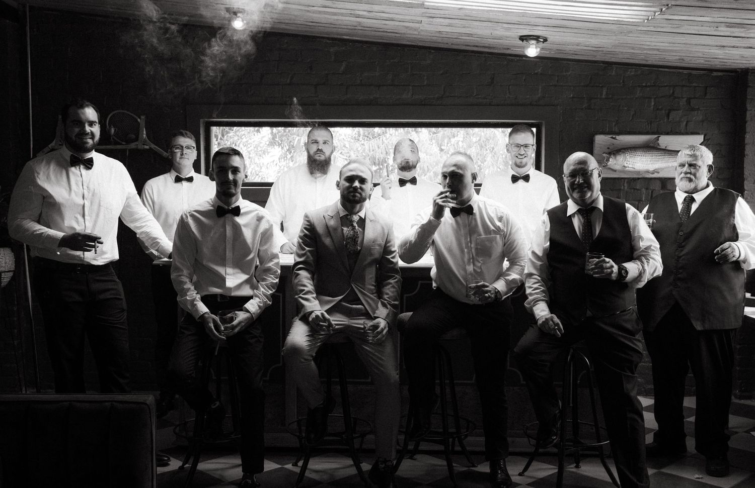 Black and white photo of groomsmen sitting together at a bar in formal attire.