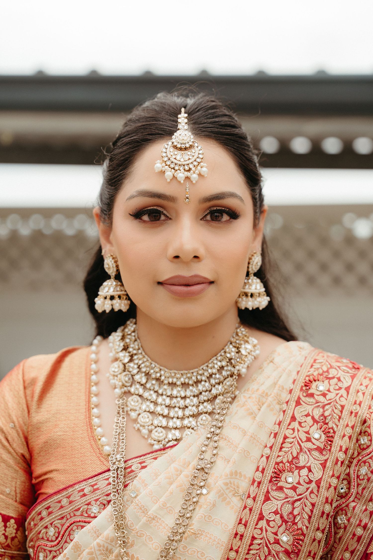 Traditional Indian bridal jewelry featuring ornate pearl and gold necklaces, earrings and forehead tikka with red and peach attire.