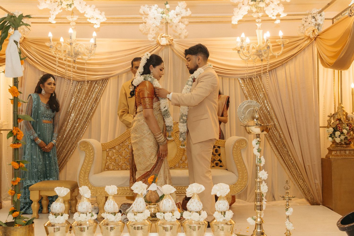 A luxurious Indian wedding ceremony setup with elegant white drapes, crystal chandeliers and traditional decor elements.