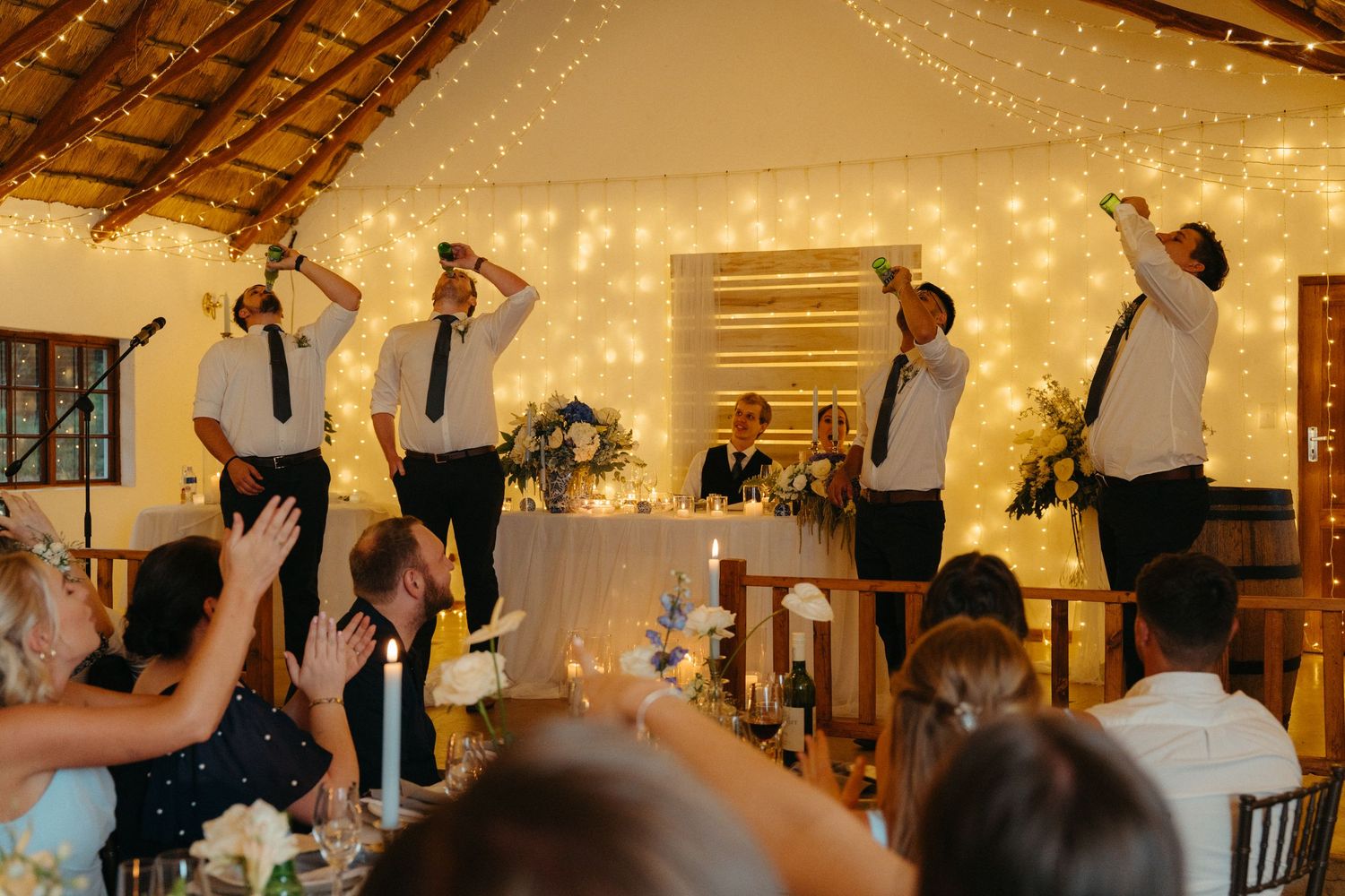 People dancing in a festive indoor venue decorated with warm glowing string lights on the ceiling.