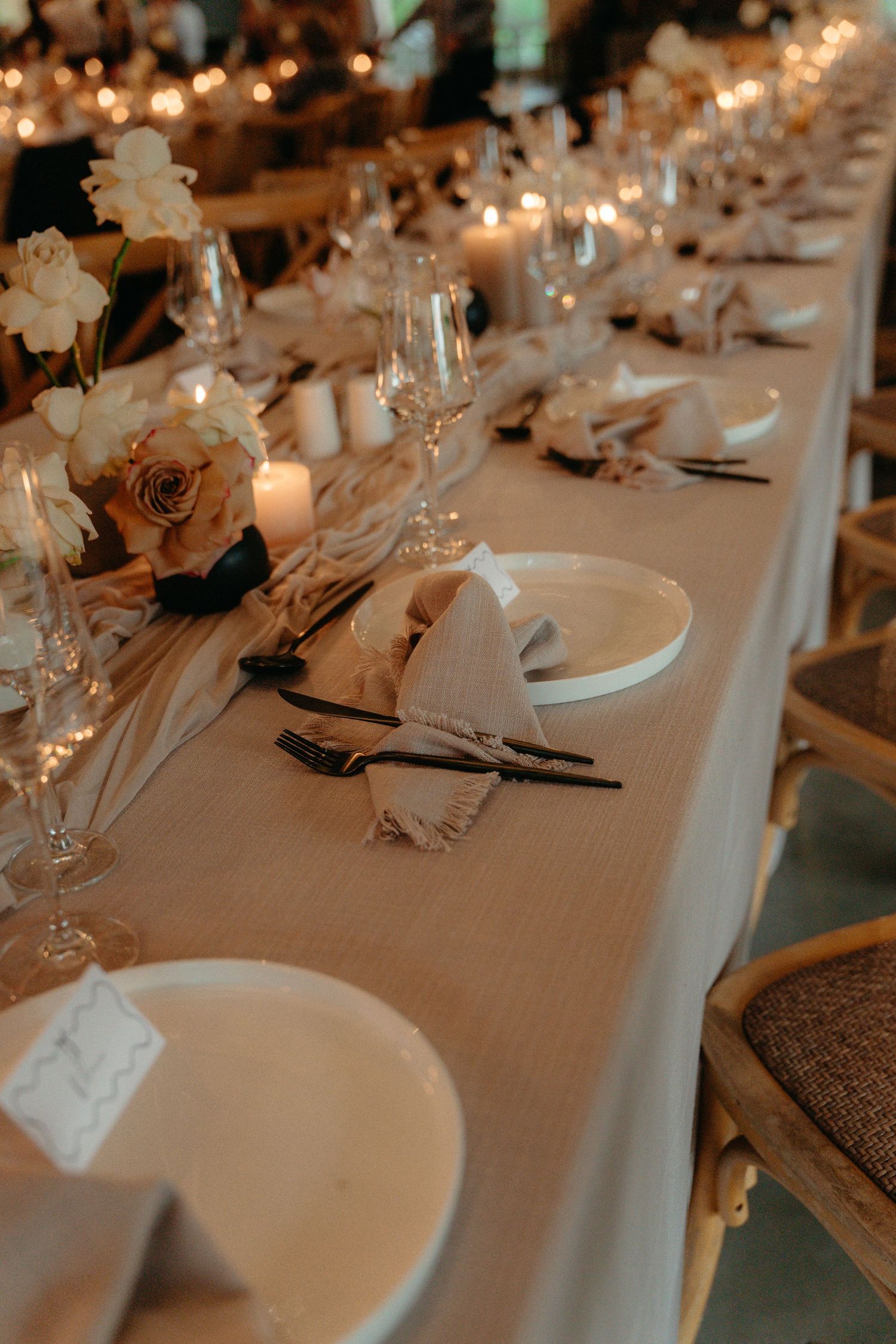 Elegant wedding reception table setting with white plates, floral centerpieces and warm ambient lighting.