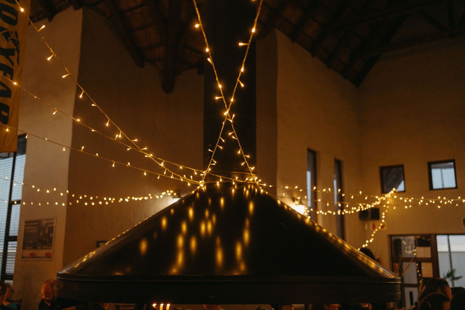 Warm string lights create a magical ceiling in a rustic reception venue.