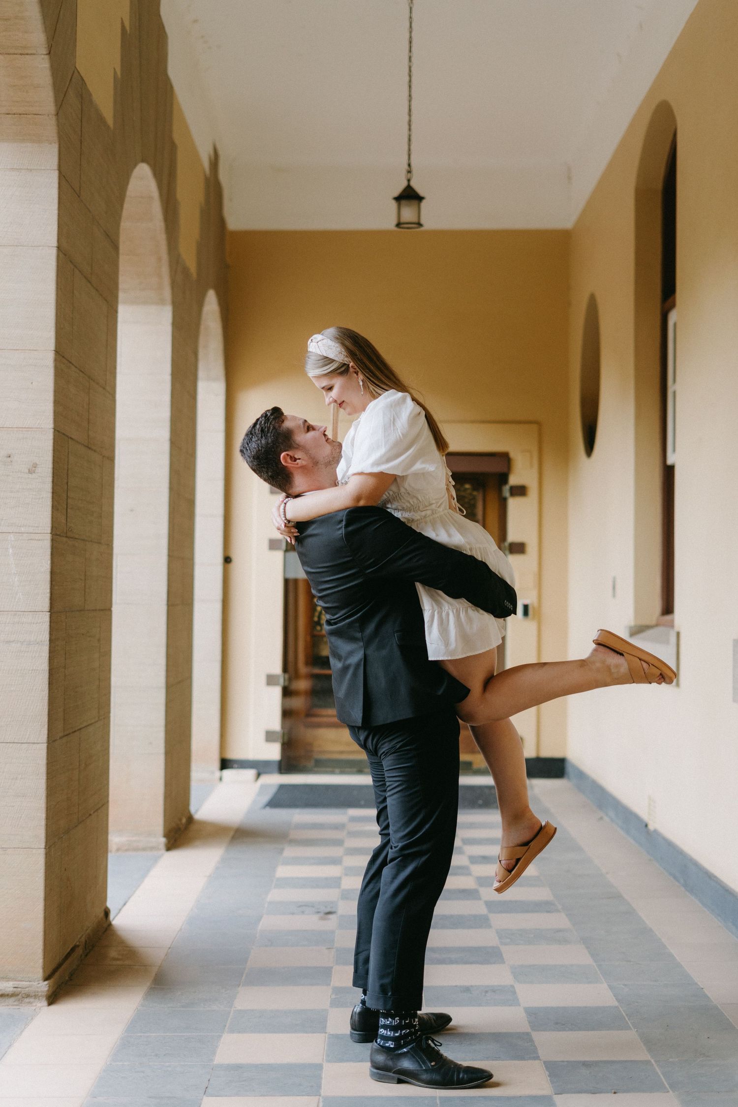 A romantic moment shared in an elegant hallway with arched columns and checkered floor tiles.