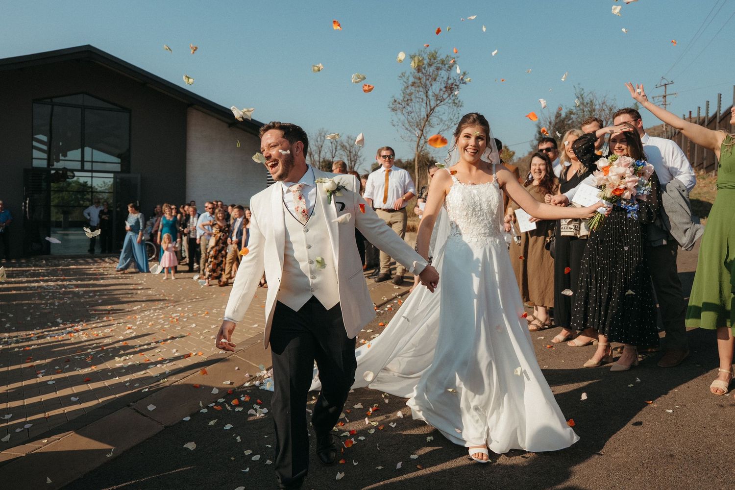 Newlywed couple walks through petal toss at the Barn @ Redstone exit with cheering guests lining the path.