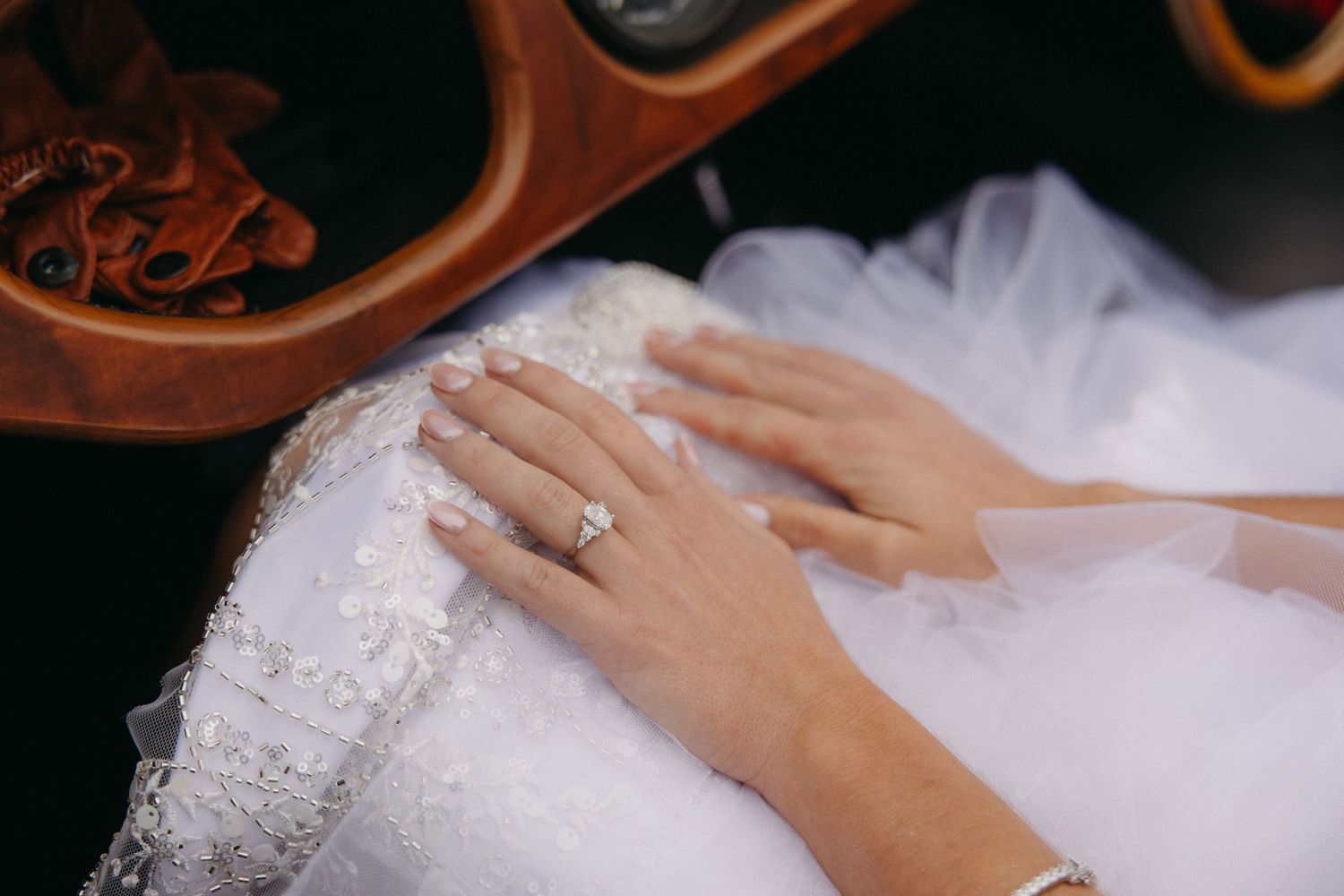 Bride's hands with diamond engagement ring and lace wedding dress detail in a vintage car.
