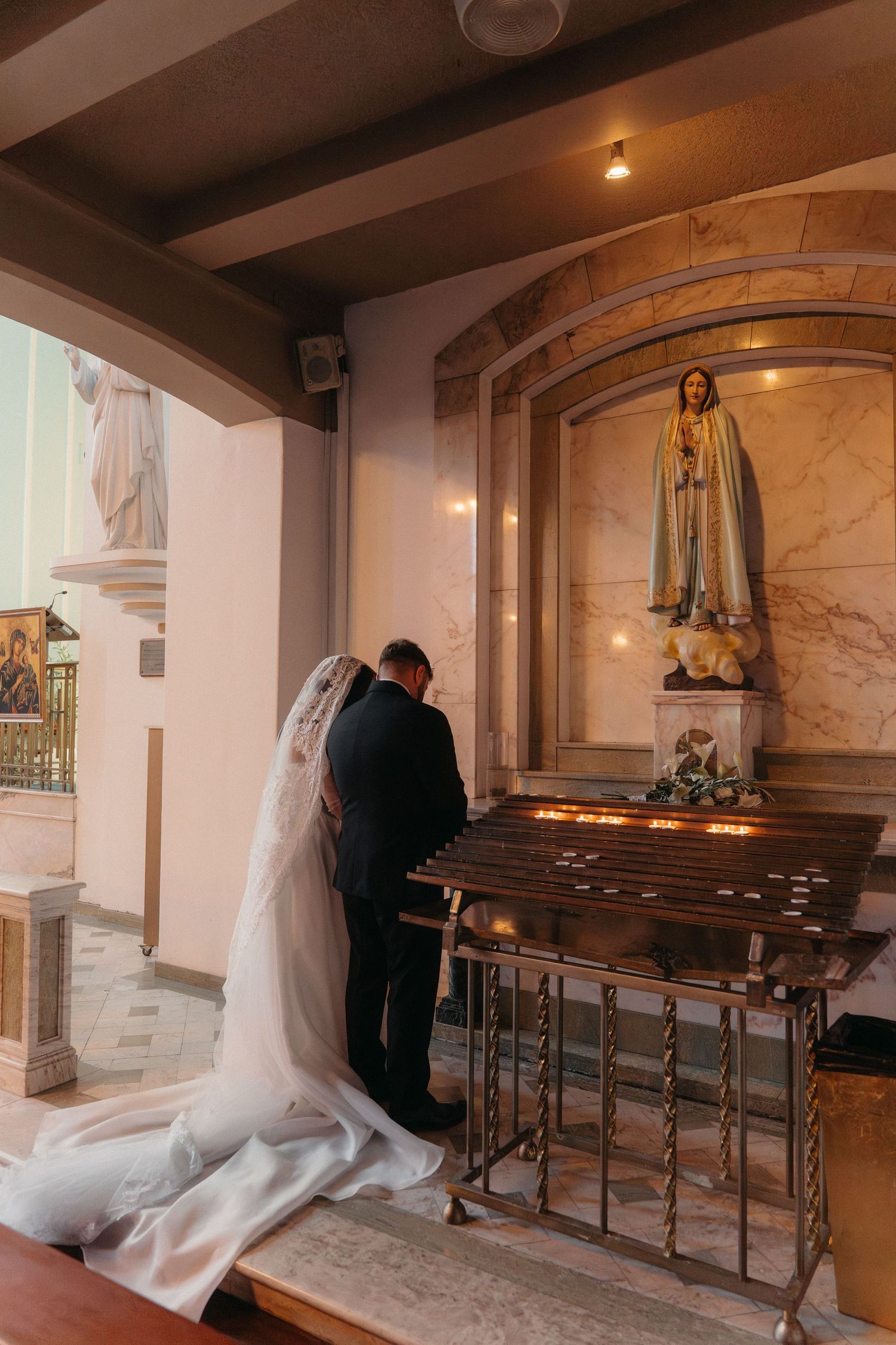 Bride and groom praying before a Virgin Mary statue with candles in Rosebank Catholic Church